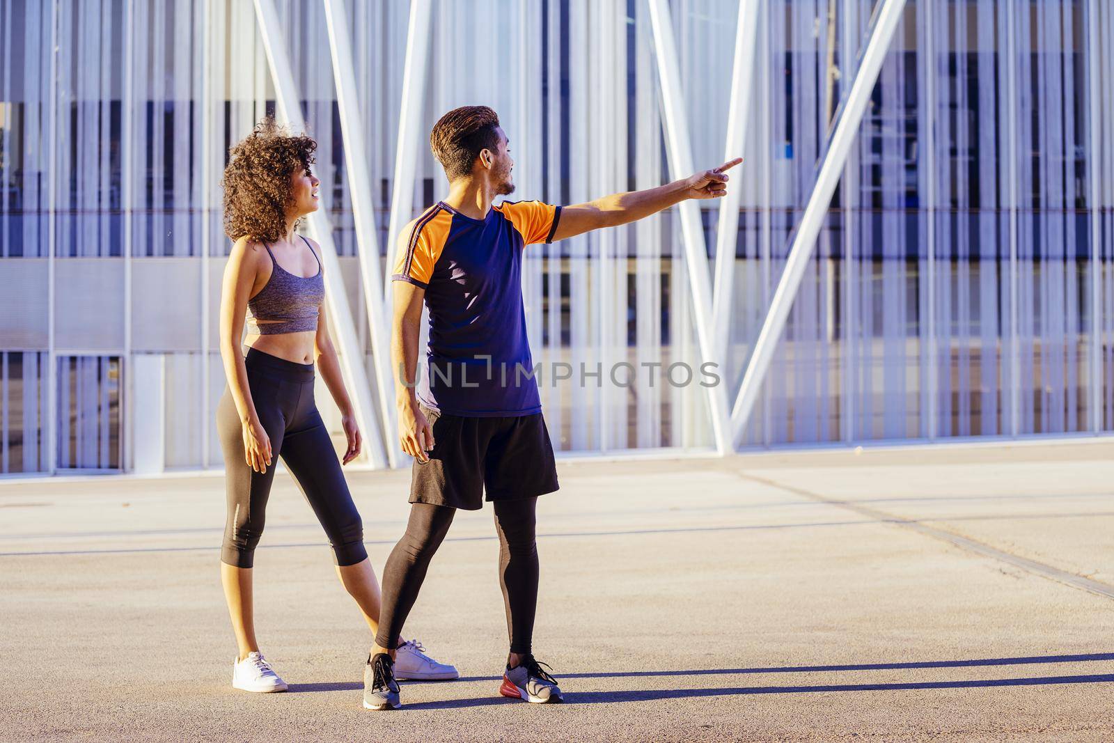 beautiful latin woman and sporty black man getting ready to run together in the city street with a building in the background. urban sports workout in couple and healthy lifestyle concept