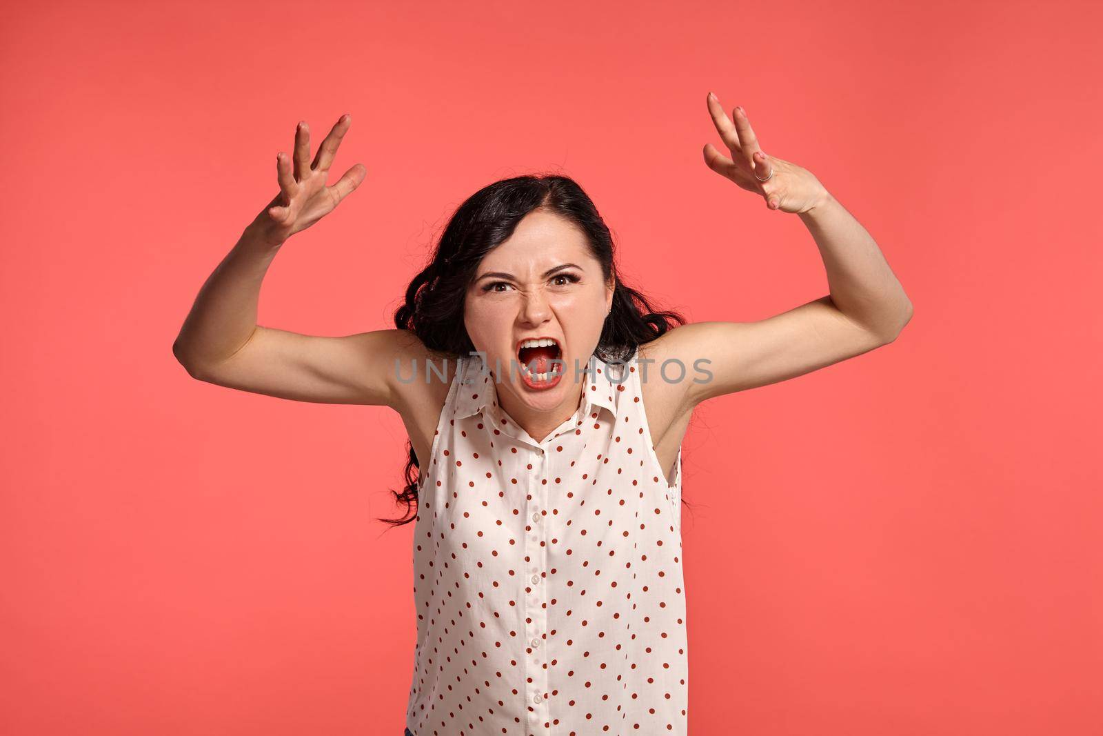Studio shot of an adorable adolescent girl looking mad, wearing casual white polka dot blouse. Little brunette posing over a pink background. People and sincere emotions.