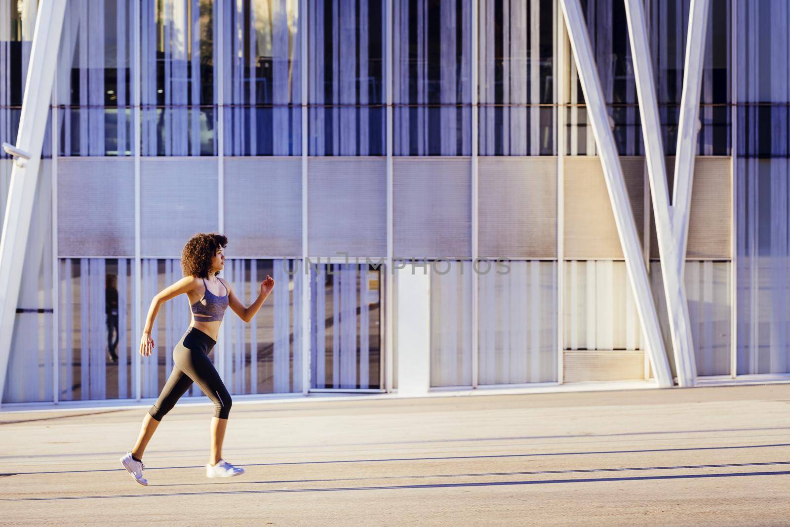 athletic latin woman running in the city street with a building in the background. urban sports workout in couple and healthy lifestyle concept