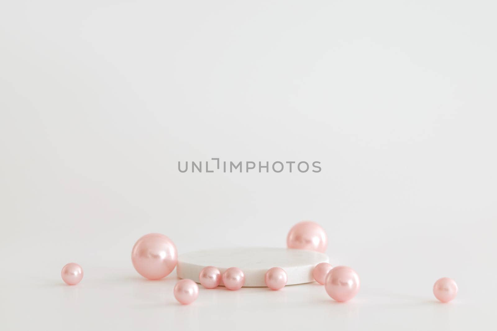 White marble podium on the white background with pink pearls. Podium for product, cosmetic presentation. Creative mock up. Pedestal or platform for beauty products