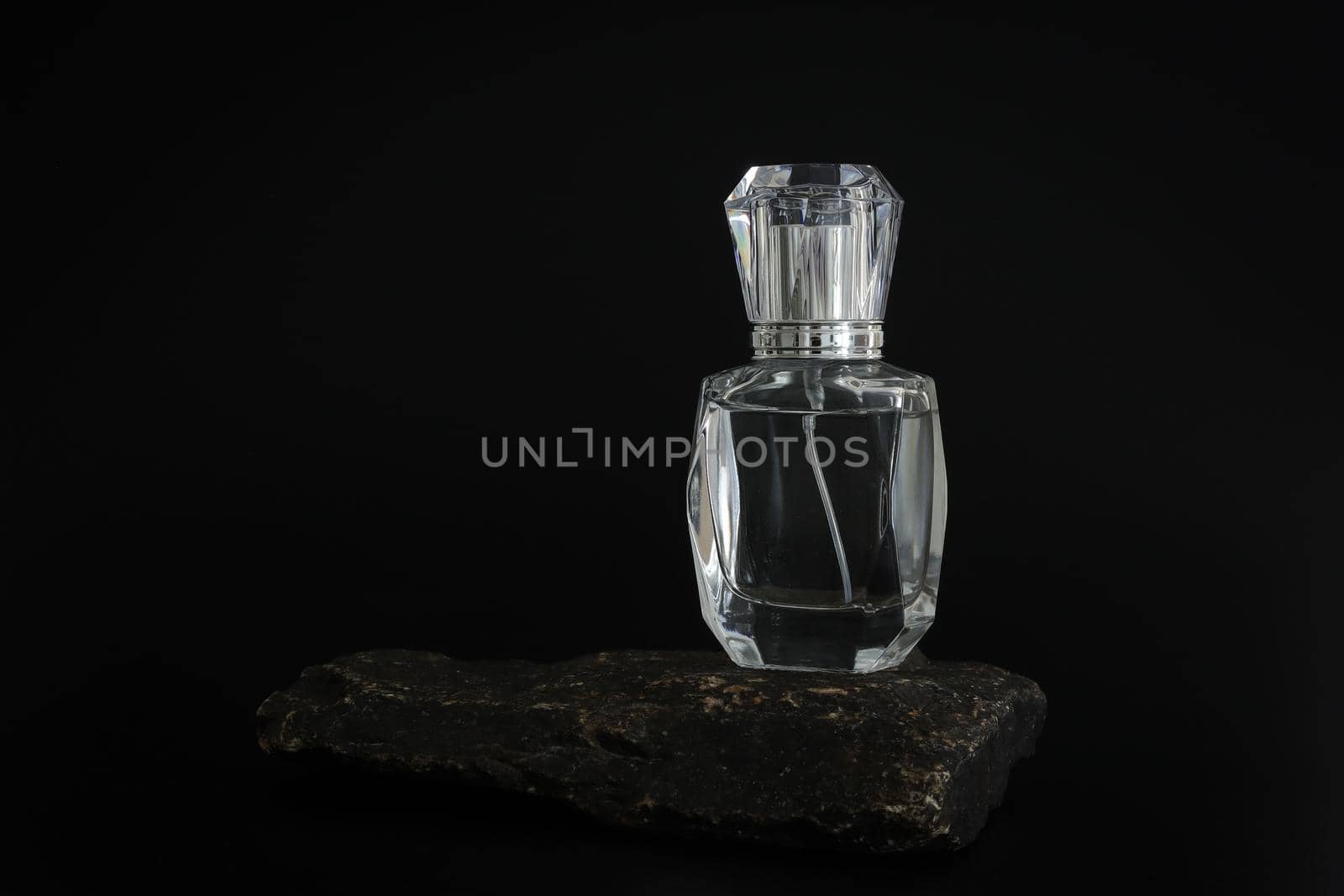 Unbranded perfume bottle standing on stone podium. Perfume presentation on the black background. Mockup. Trending concept in natural materials. Women's and men's essence. Natural cosmetic