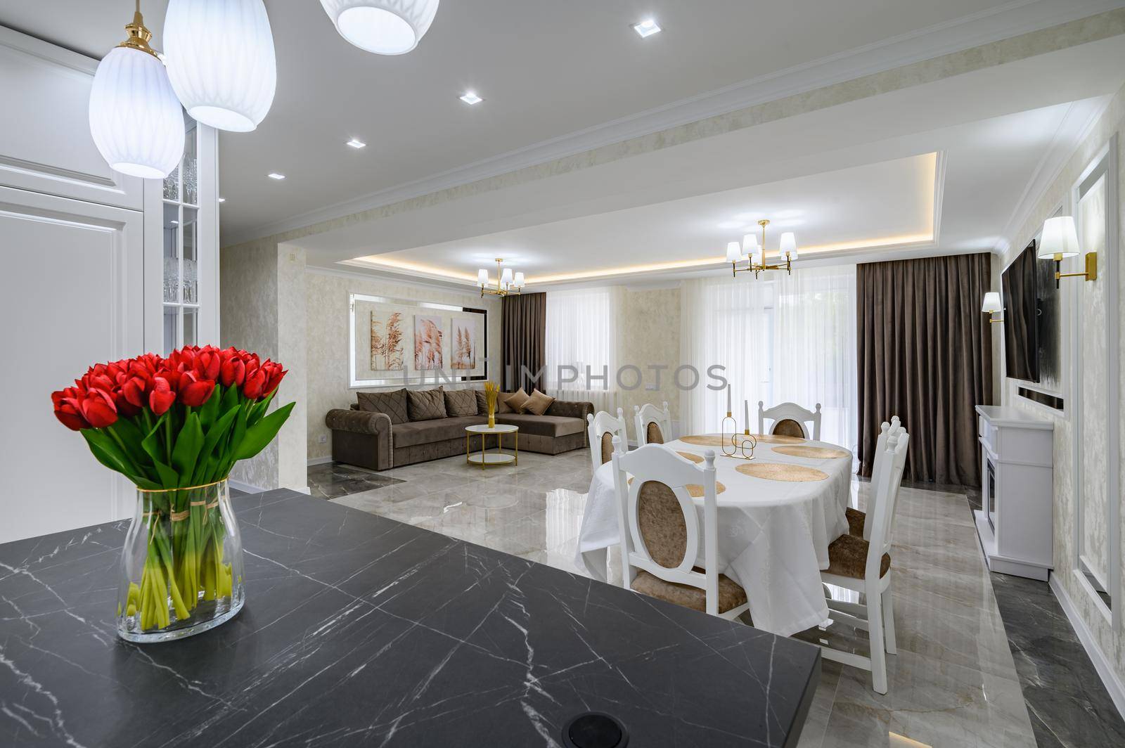 Luxurious white large modern studio interior with kitchen, black marble countertop over kitchen island, dining area with served table