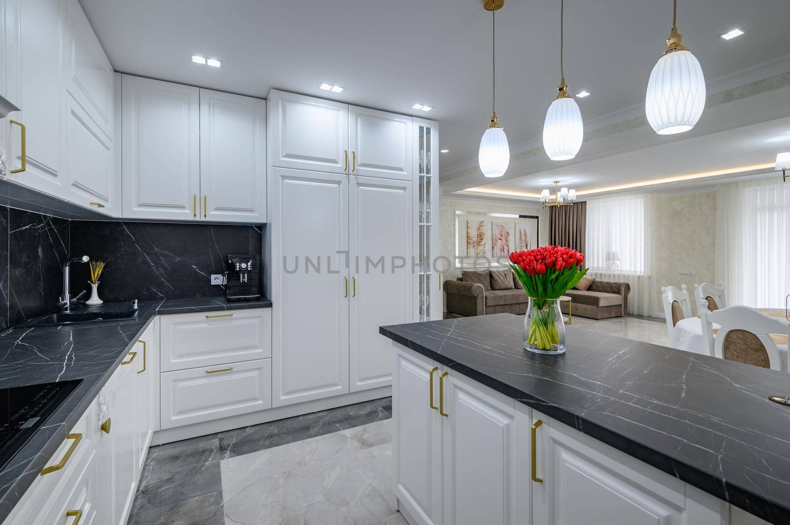 Large black and white expensive well-designed modern kitchen in studio interior, black marble countertop on kitchen island with bouquet of red flowers