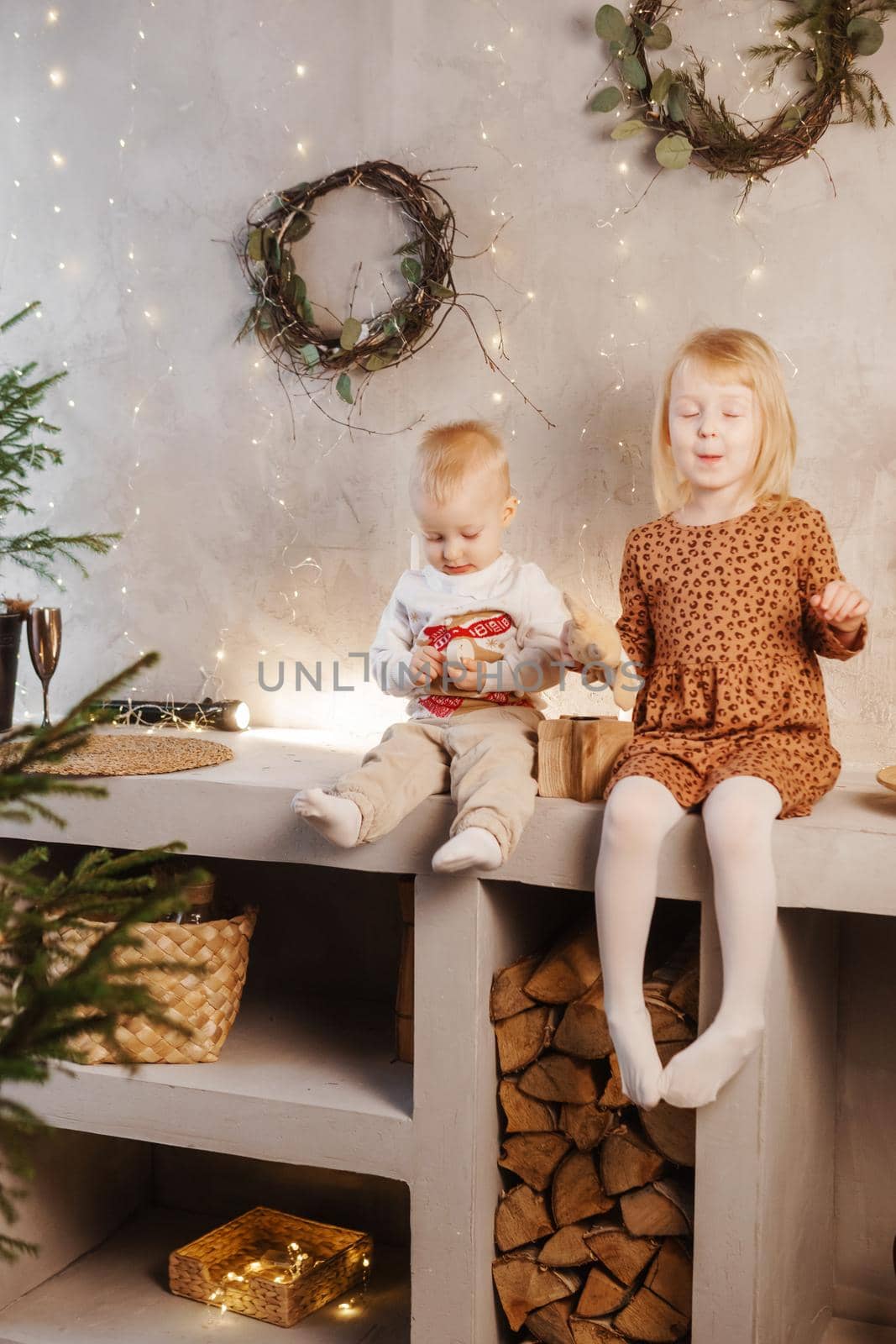 Little brother and sister play on Christmas eve in a beautiful house decorated for the New Year holidays. Children are playing with a Christmas gift. Scandinavian-style interior with live fir trees and a wooden staircase.