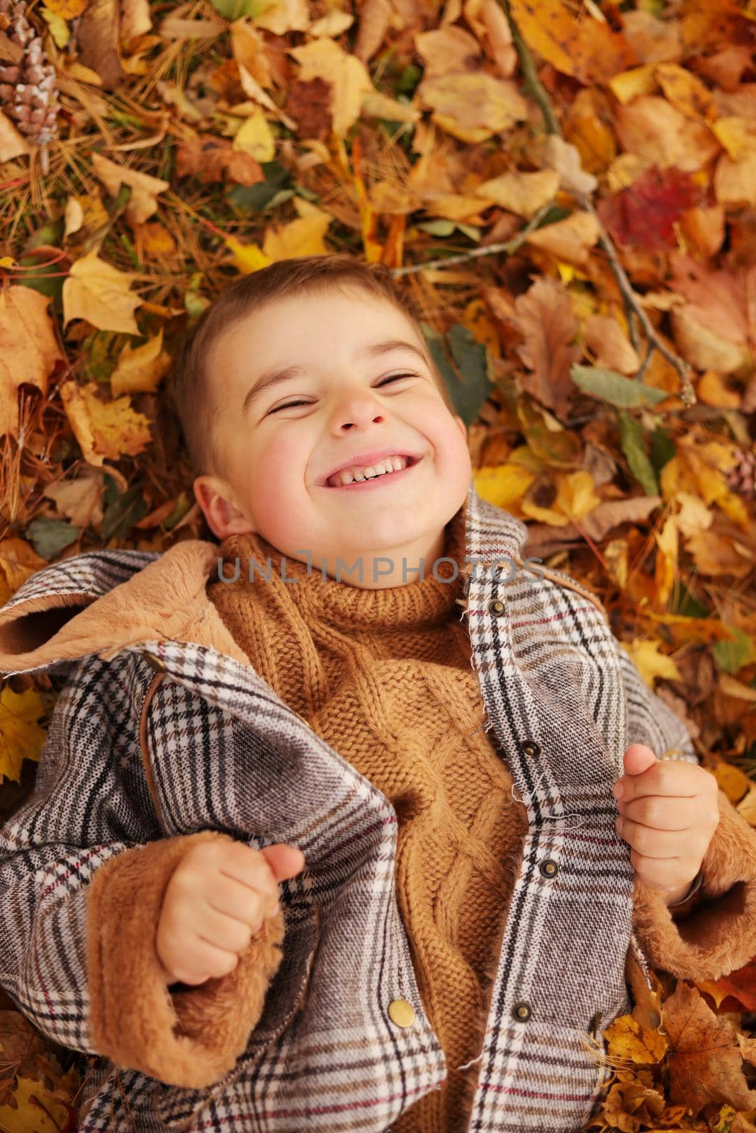 Outdoor fun in autumn. Child playing with autumn fallen leaves in park. Happy little boy lying down on yellow leaves outdoors. View from above