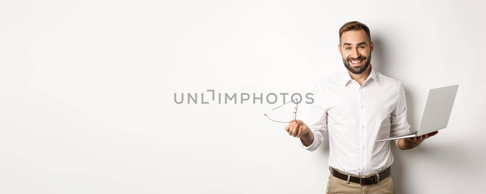 Professional confident businessman doing job on laptop, looking satisfied, standing over white background.