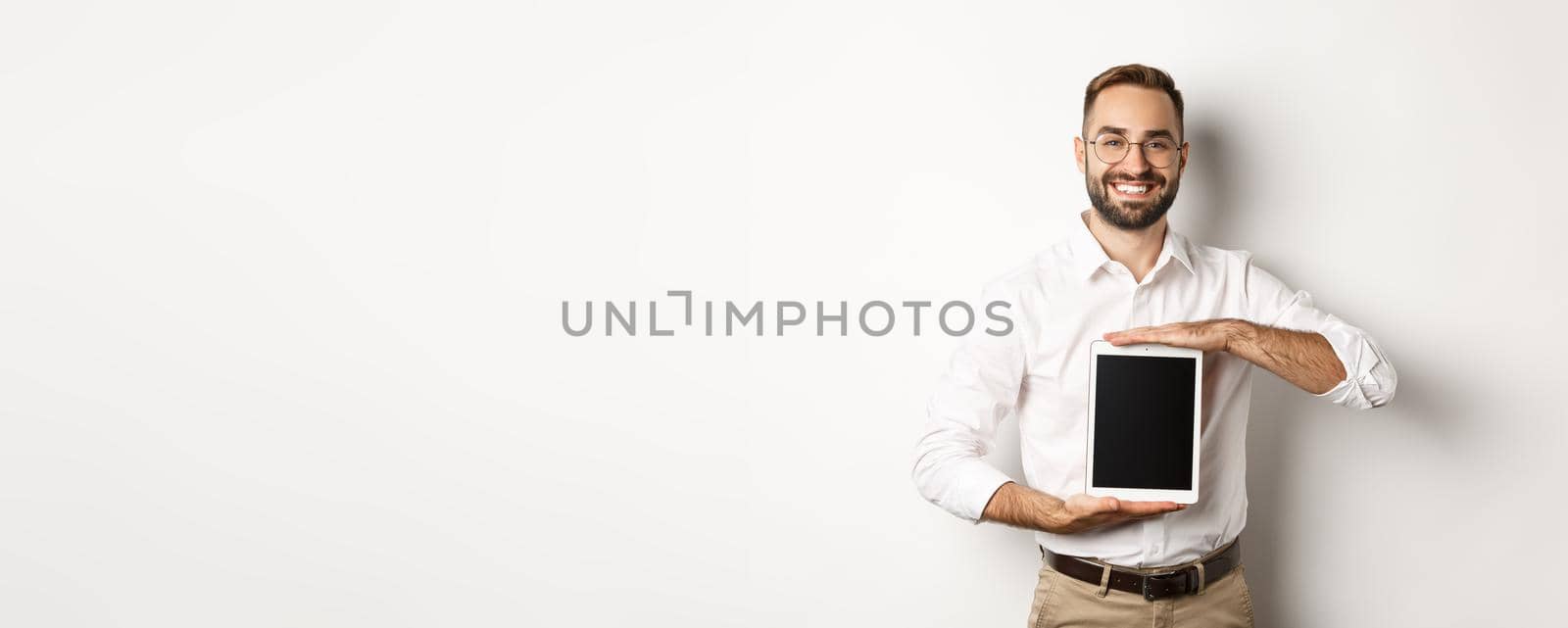 Smiling manager showing something on digital tablet screen, demonstrating website, standing over white background.