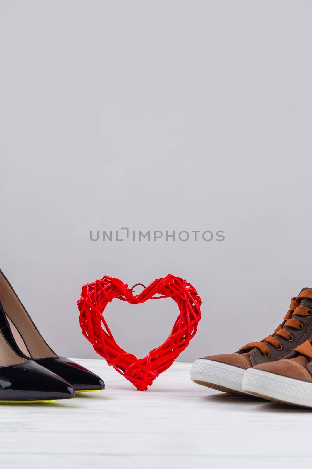 Still life of mens and womens shoes and red heart. Vertical shot copy space.