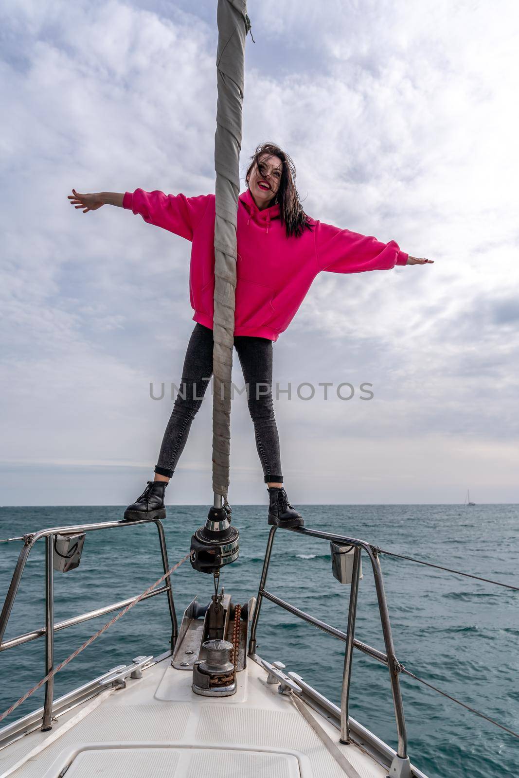 Woman standing on the nose of the yacht at a sunny summer day, breeze developing hair, beautiful sea on background.