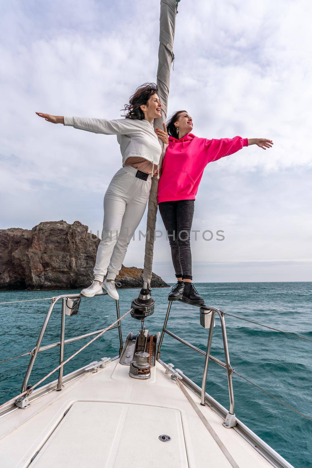 Two women standing on the nose of the yacht on a sunny summer day, the breeze develops hair, a beautiful sea against the background.