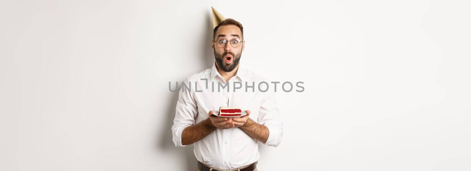 Holidays and celebration. Happy man having birthday party, making wish on b-day cake and smiling, standing against white background.