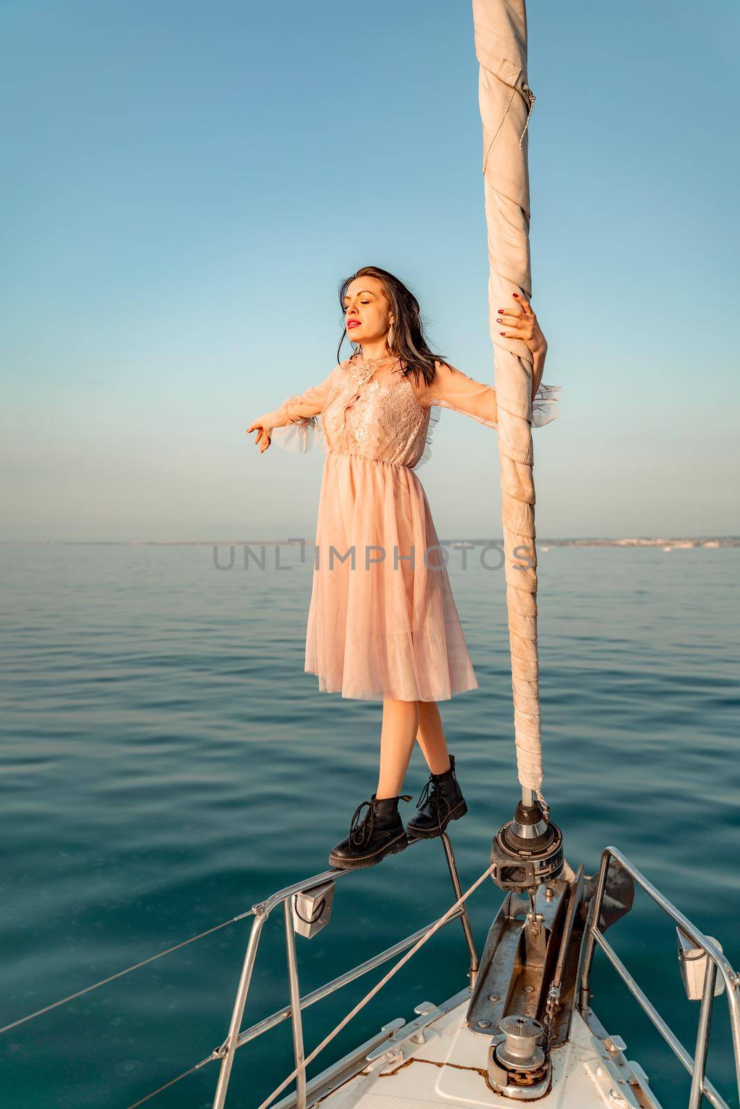 Woman standing on the nose of the yacht at a sunny summer day, breeze developing hair, beautiful sea on background by Matiunina