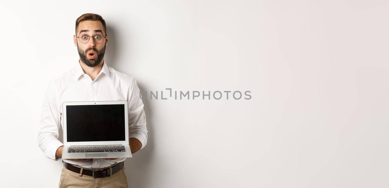 Excited businessman showing something on laptop screen, standing happy over white background.