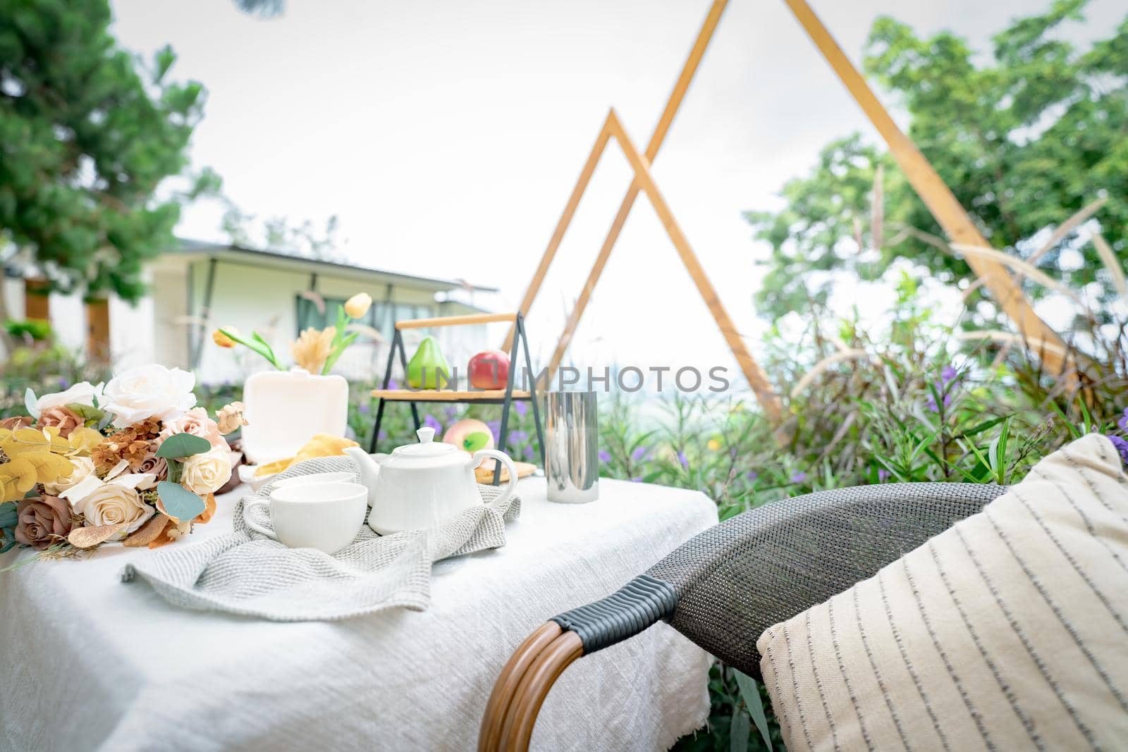 Coffee cup and flowers bouquet on table in garden. Afternoon tea concept. Home outdoor furniture. Wicker chair and table with white tablecloth in vintage style. Cozy chair and table on the terrace.