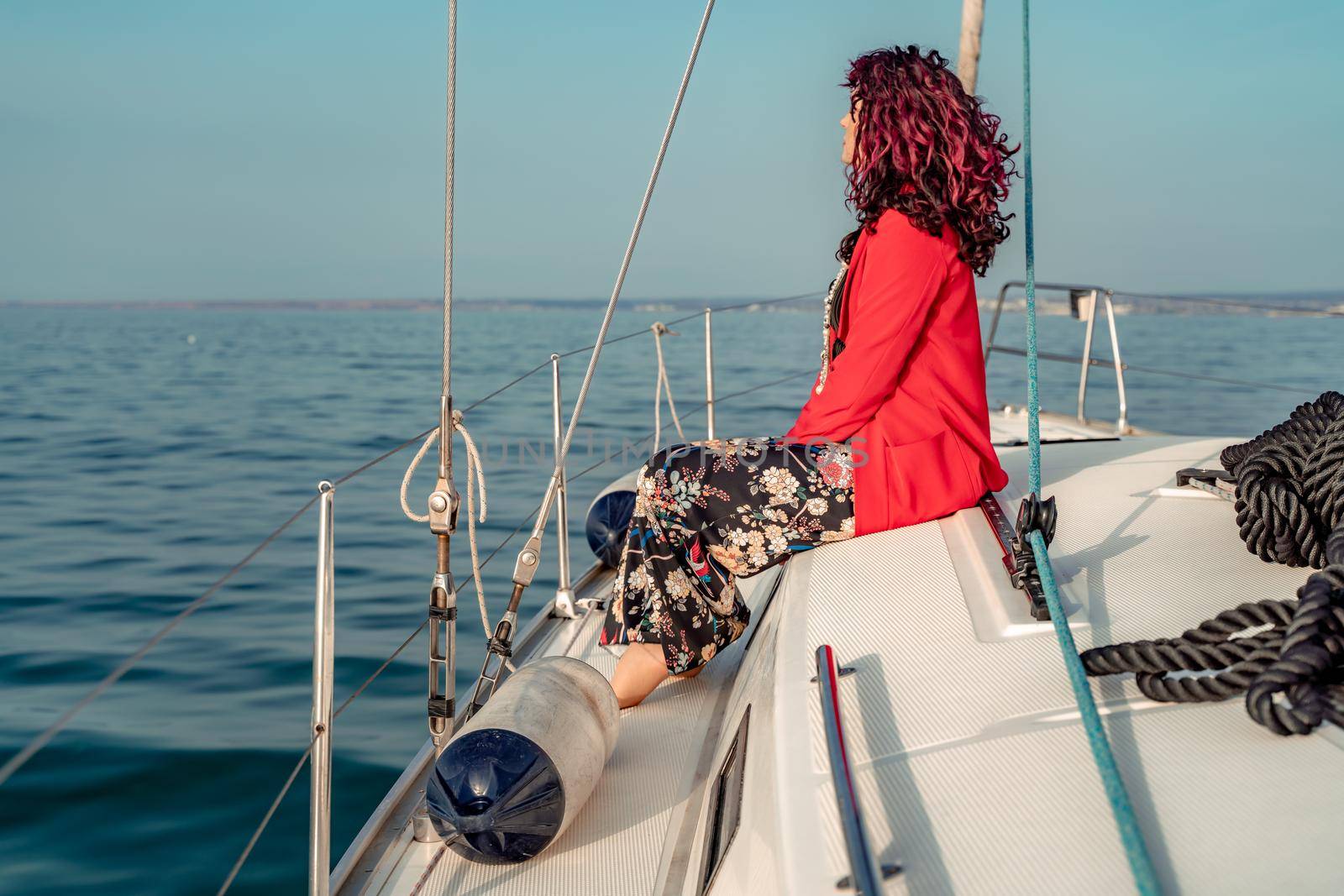 A woman sits on the bow of a yacht on a sunny summer day, the breeze develops her hair, a beautiful sea is in the background by Matiunina