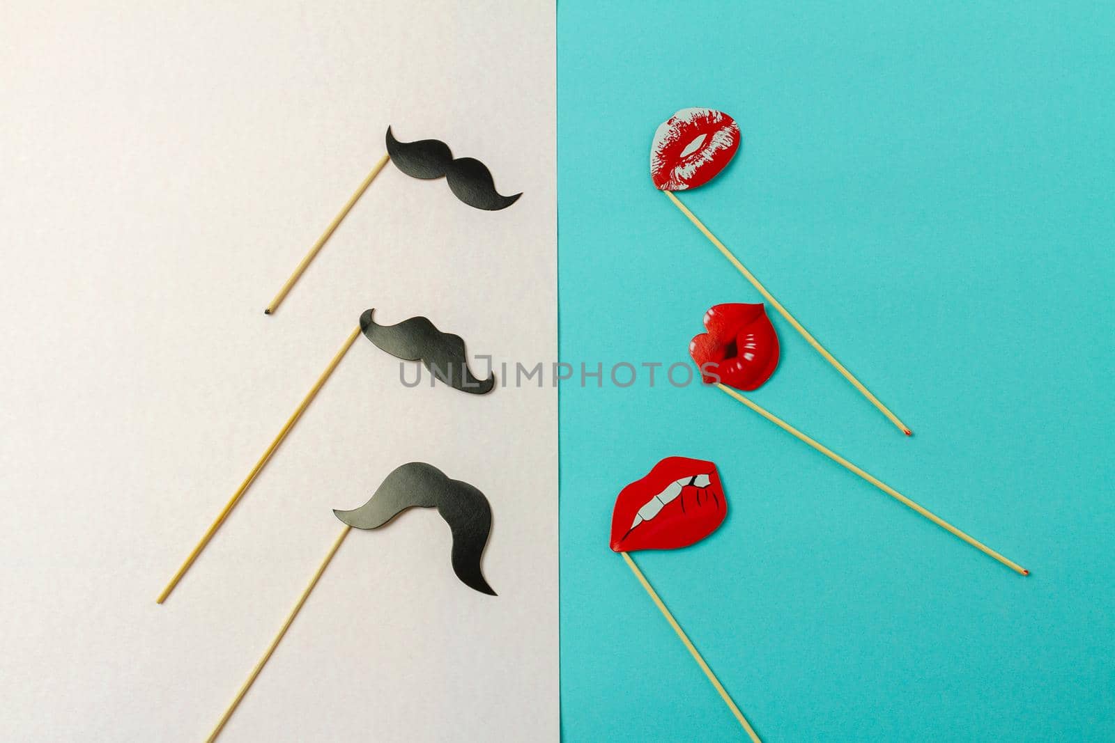 Paper moustaches and lips on wooden sticks. White and turquoise background.