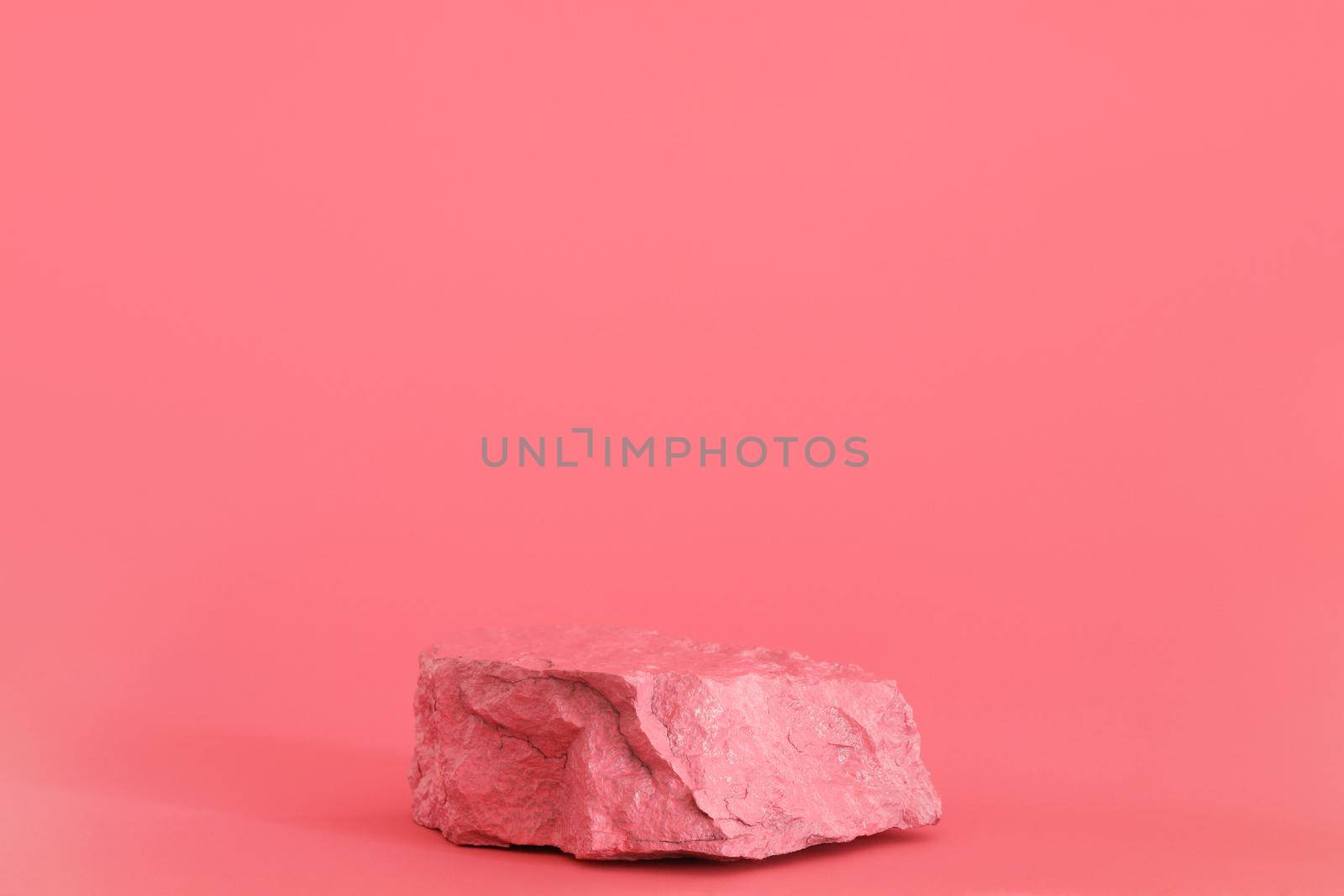 Pink stone, rock podium on the pink background. Podium for product, cosmetic presentation. Creative mock up. Pedestal or platform for beauty products