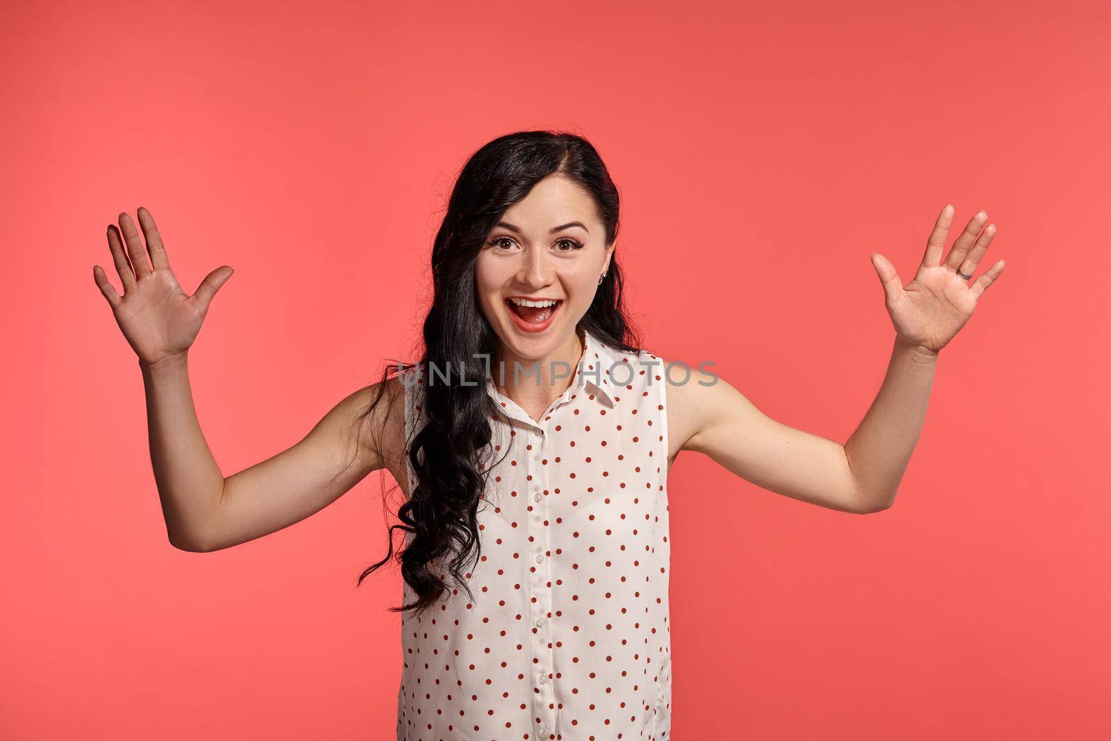 Studio shot of a gorgeous girl teenager, wearing casual white polka dot blouse. Little brunette female is smiling and looking very happy, posing over a pink background. People and sincere emotions.