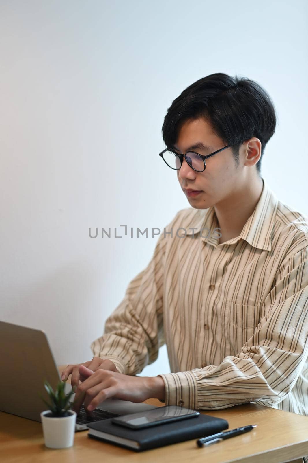 Young man in eyeglasses working with laptop in office. by prathanchorruangsak