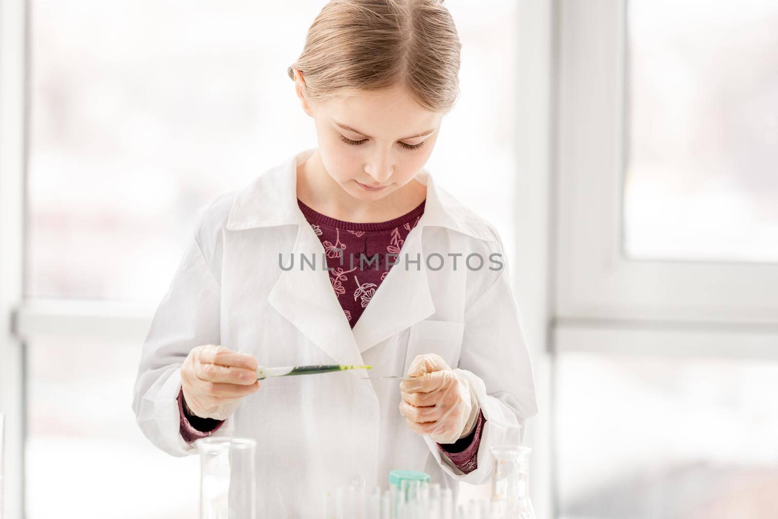 Smart girl during scientific chemistry experiment looking at glass with tests. Schoolgirl with chemical equipment on school lesson