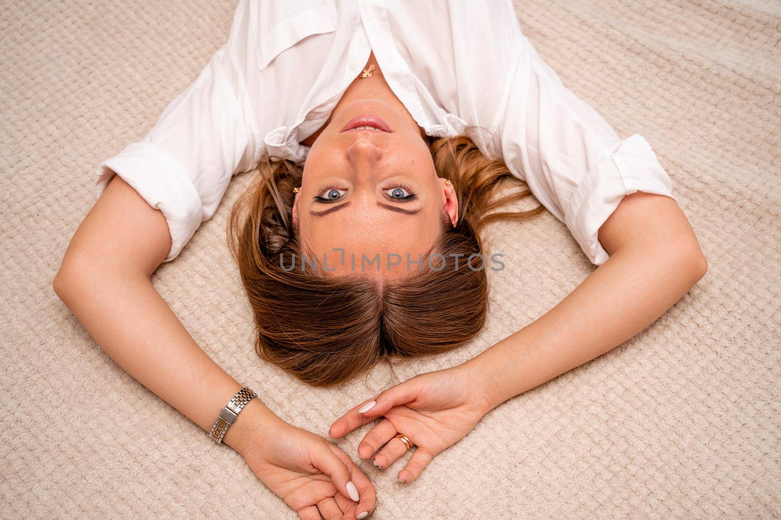 The woman lies on the bed on her back, top view. She looks straight ahead, wearing a white shirt by Matiunina