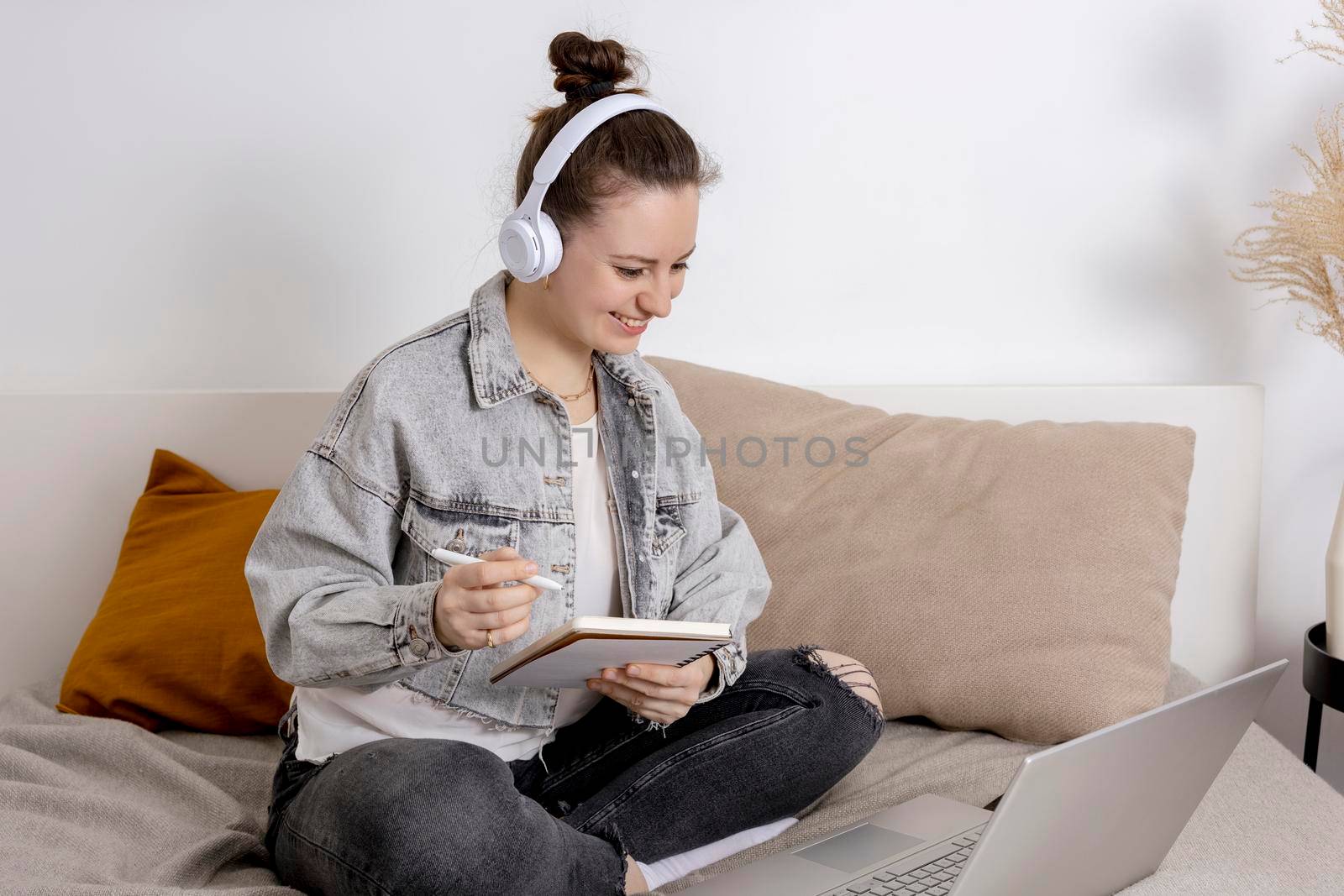 Young beautiful woman with casual clothes sitting on the bed at home with laptop computer and studying. Girl using e-learning platform to make a video call with her teacher. Distance education