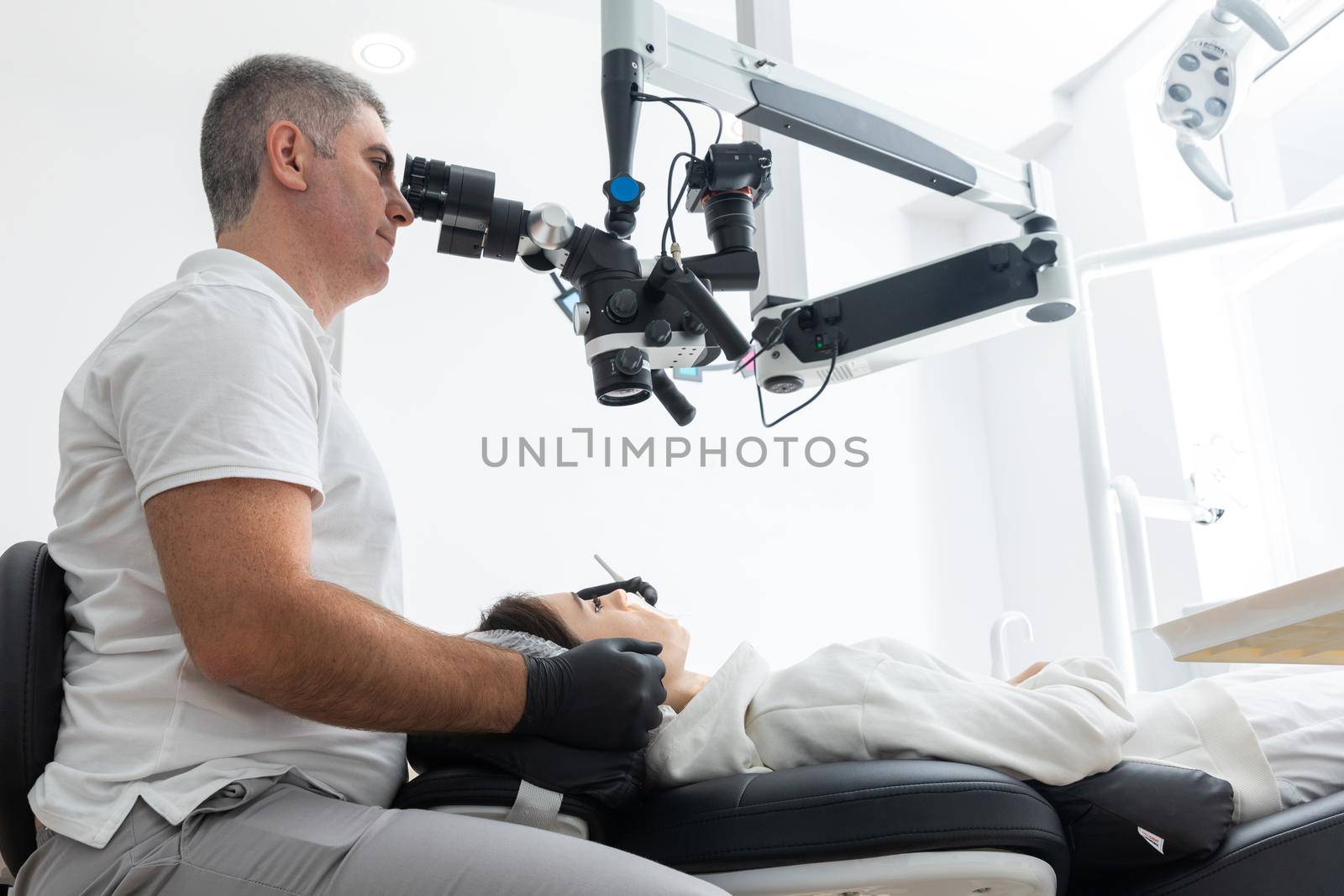 Male dentist using dental microscope treating patient teeth at dental clinic office. Medicine, dentistry and health care concept