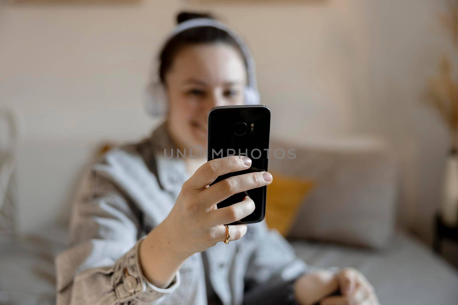 Young beautiful woman with casual clothes sitting on the bed at home and making selfie on smartphone. Girl using mobile phone to surf in internet, make video call, talk with friends. Influencer. by creativebird