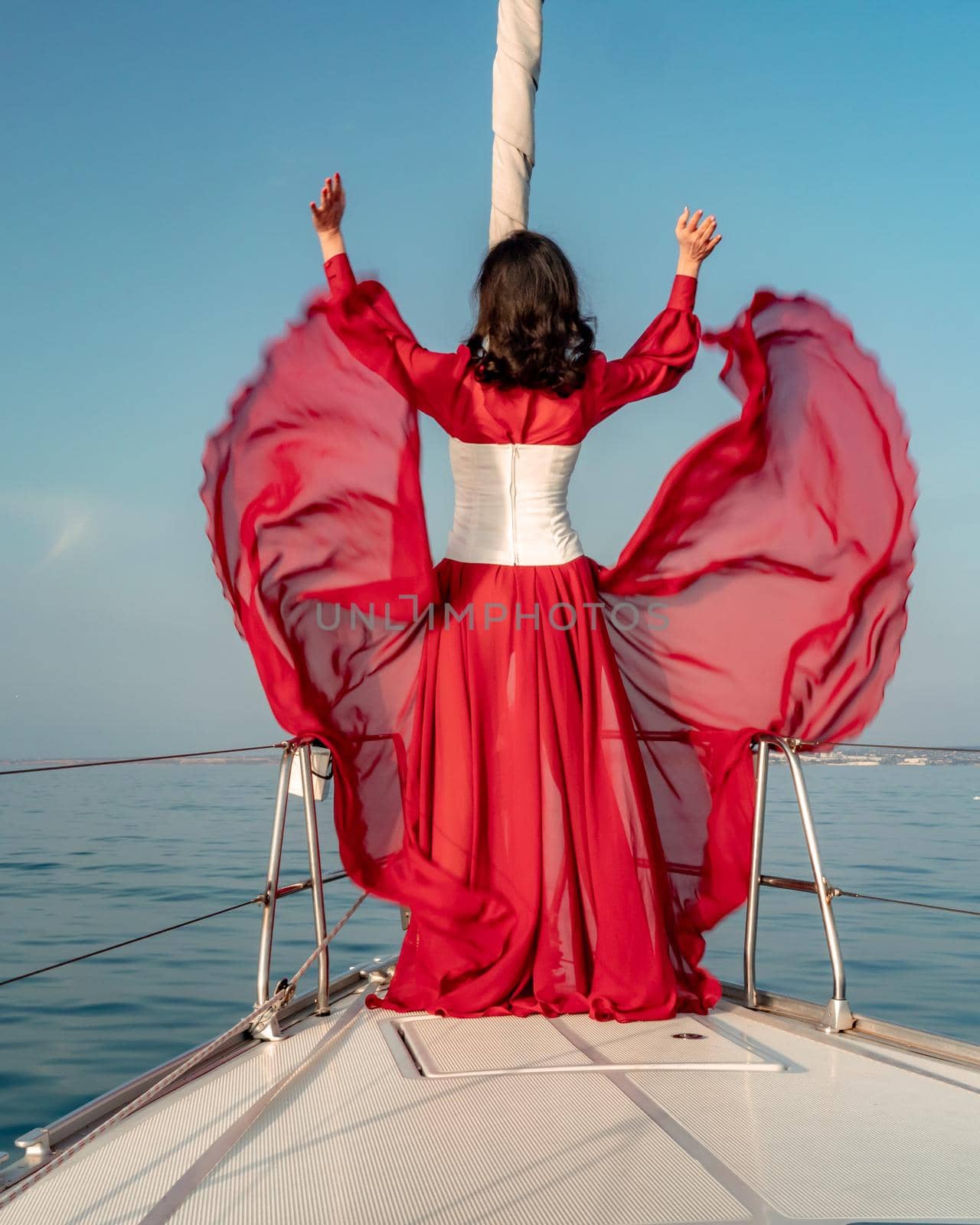 Attractive middle-aged woman in a red dress on a yacht on a summer day. Luxury summer adventure, outdoor activities. by Matiunina