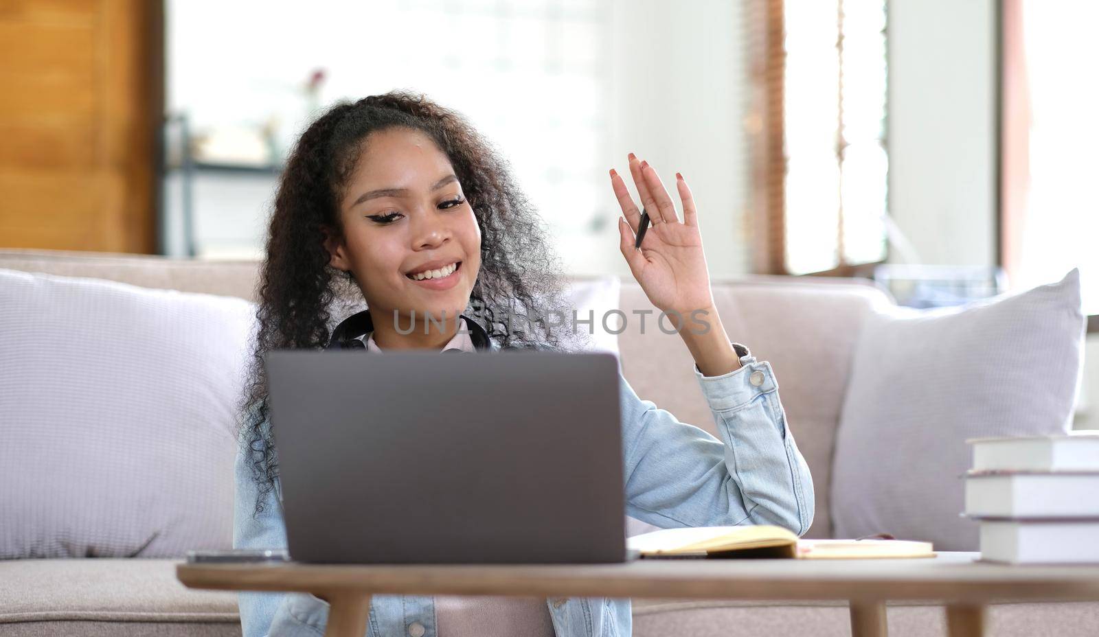 Overjoyed millennial female student in headphones look at laptop screen study online from home. Happy young mixed race woman in earphones talk on video call with teacher. Virtual event concept. by wichayada