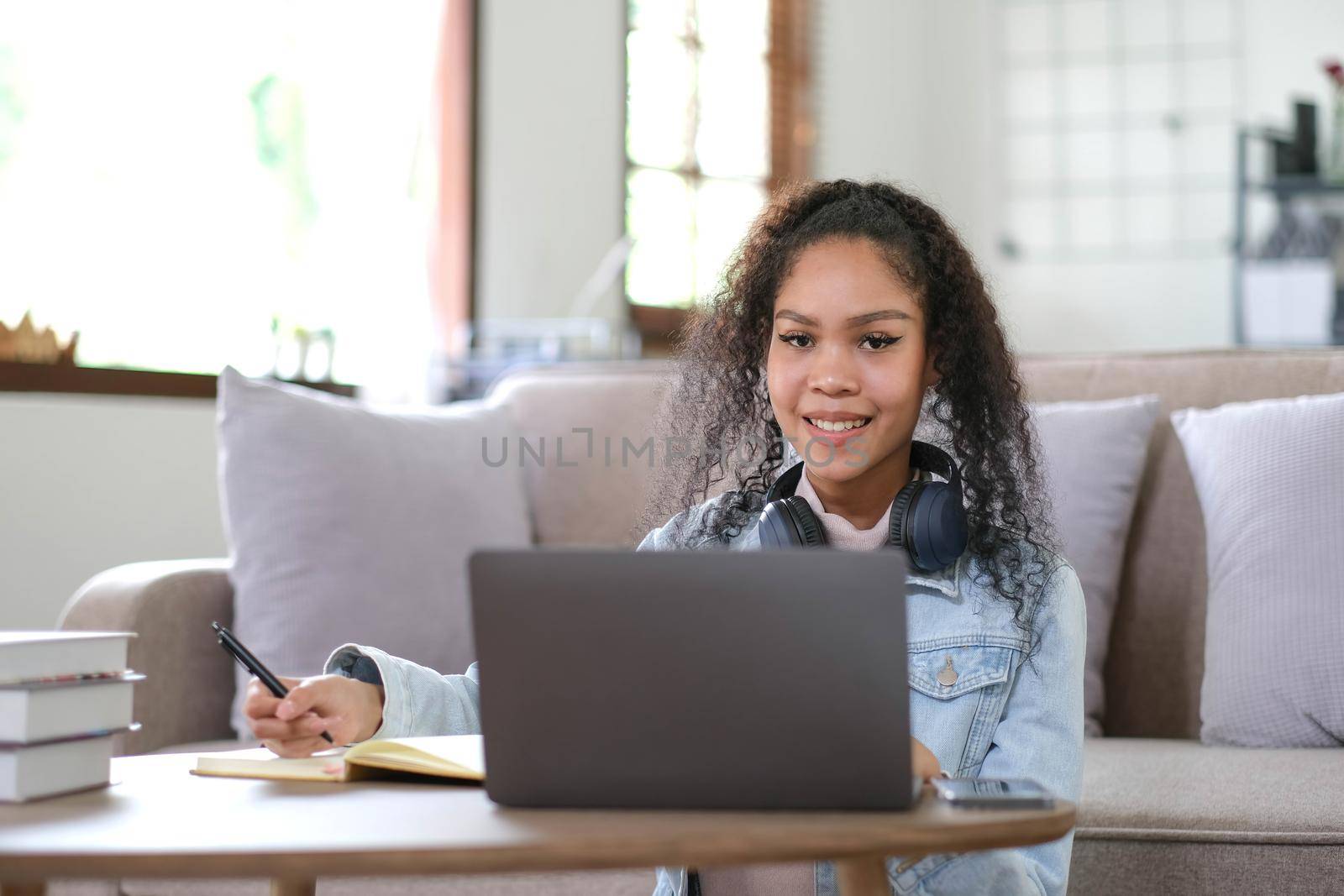Portrait of happy female student with dark skin smiling at camera. cheerful African American hipster girl enjoying e learning and preparation to course work by wichayada