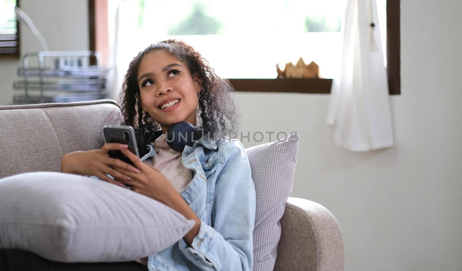 Young relaxed woman listening to the music resting on the sofa at home. Caucasian girl using smart phone and headphones for music application online..