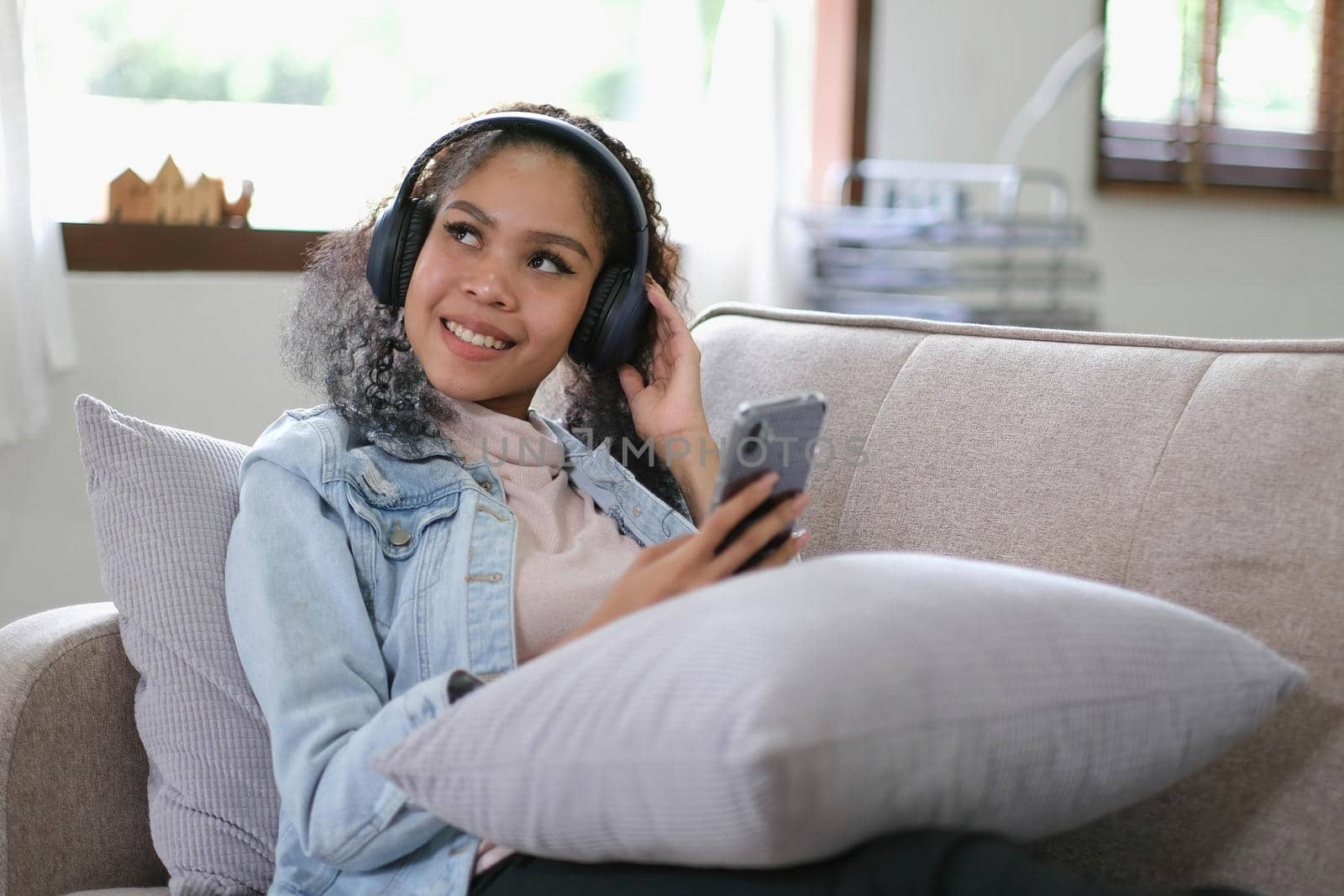 Young relaxed woman listening to the music resting on the sofa at home. Caucasian girl using smart phone and headphones for music application online. by wichayada