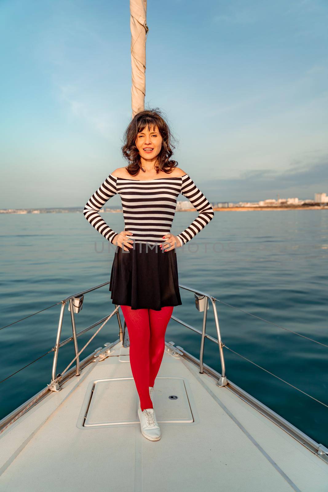 Woman standing on the nose of the yacht at a sunny summer day, breeze developing hair, beautiful sea on background by Matiunina