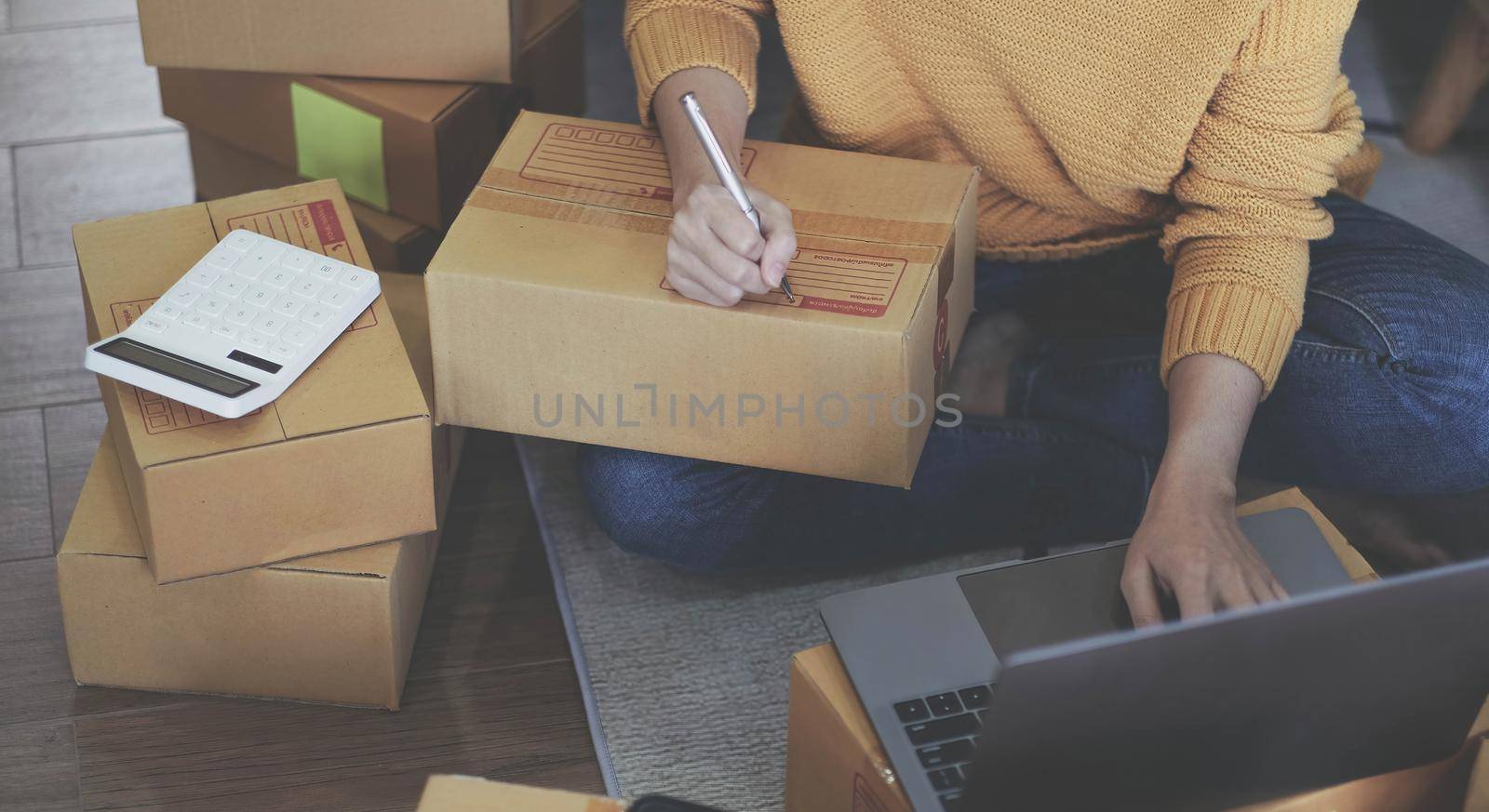 Startup Entrepreneurship Small Business SME Freelance Young lady working at home with boxes on the floor and laptop online Marketing Packaging SME Shipping Ecommerce Concepts by wichayada