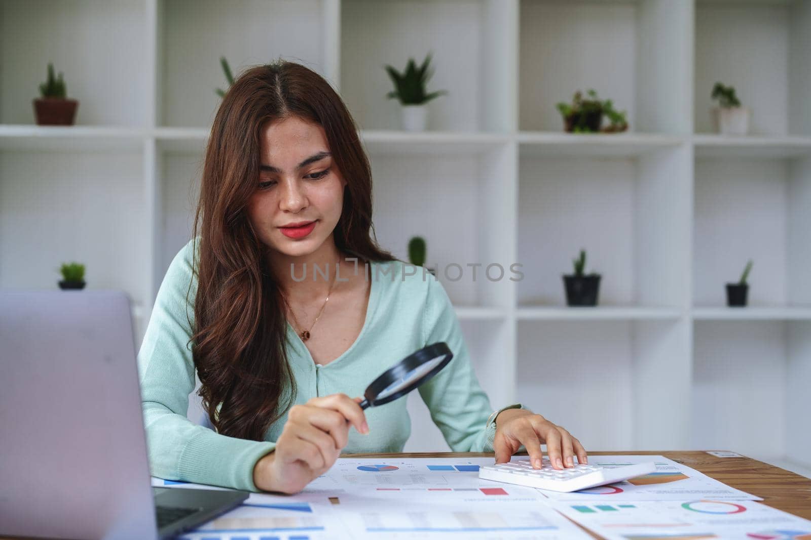 A half-bred girl, an audit employee, an accountant holding a magnifying glass and using a calculator to check the financial statement documents to calculate the annual tax payment to the IRS.