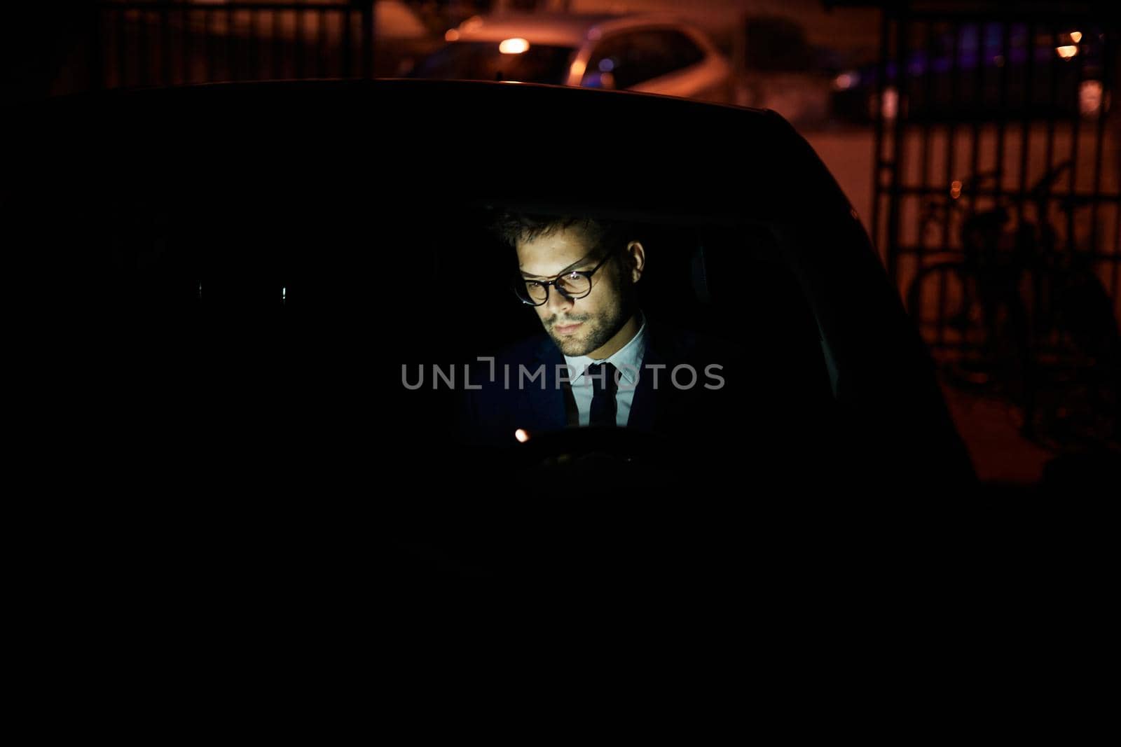 Portrait of a young businessman with tablet or laptop working late at night in office or looking at a device screen in car