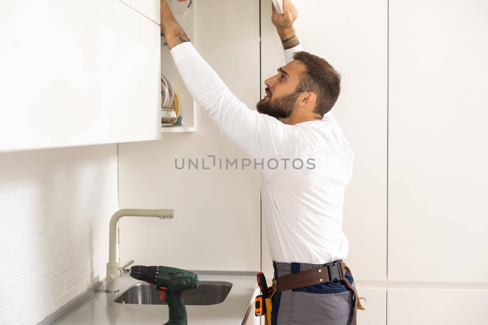 Two handymen, workers in uniform fixing, installing furniture and equipment in the kitchen, using screwdriver indoors. Furniture repair and assembly concept