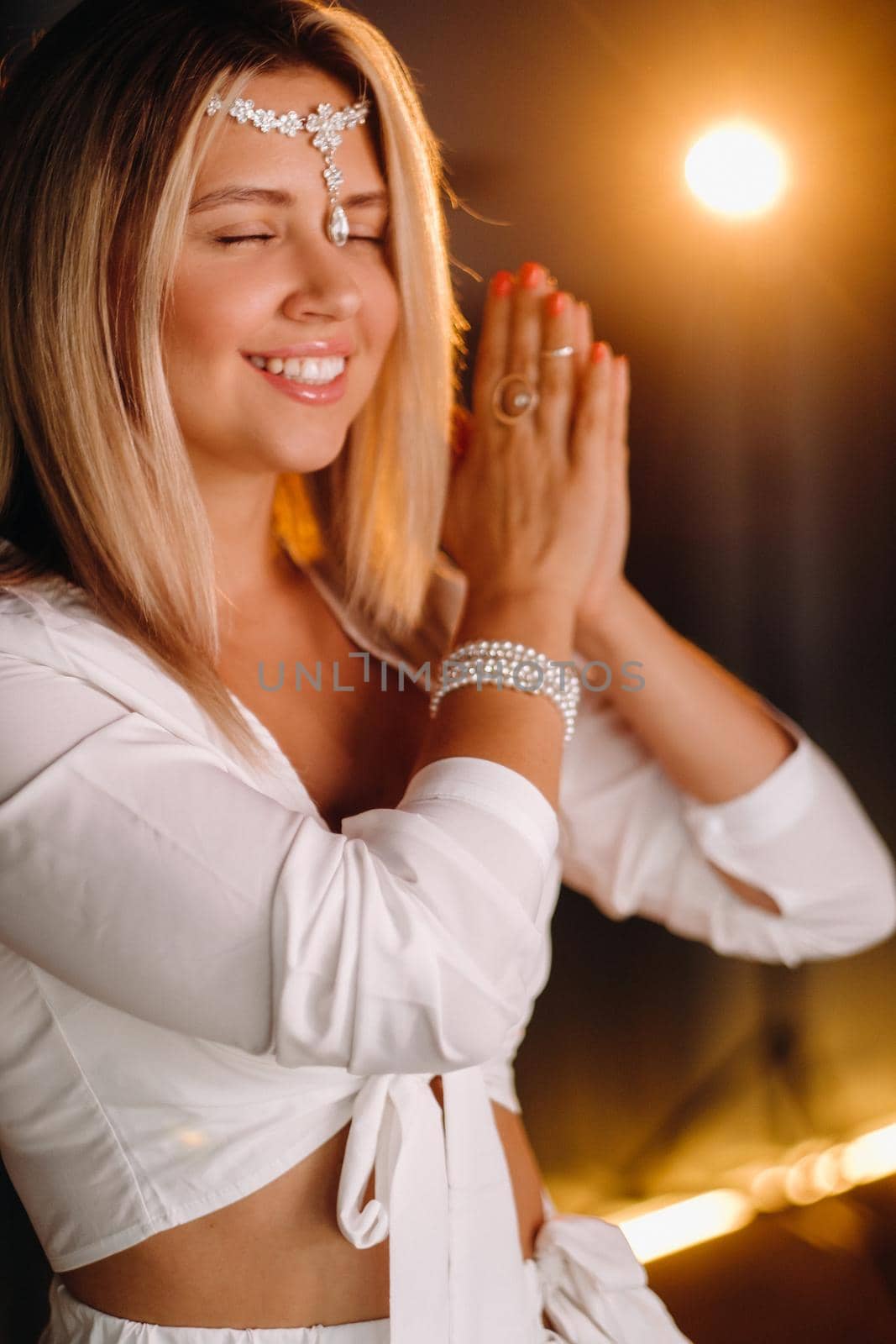 Portrait of a smiling girl in a white dress with her palms clasped in front of her.