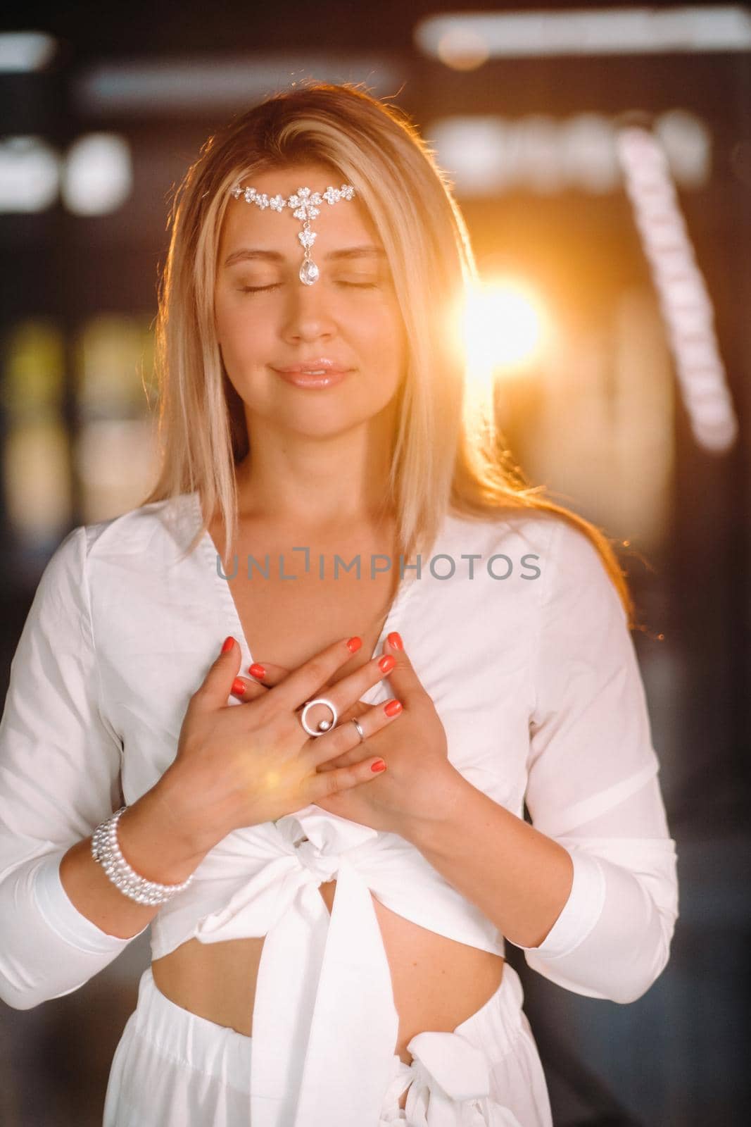 Portrait of a smiling girl in a white dress with her palms clasped in front of her.