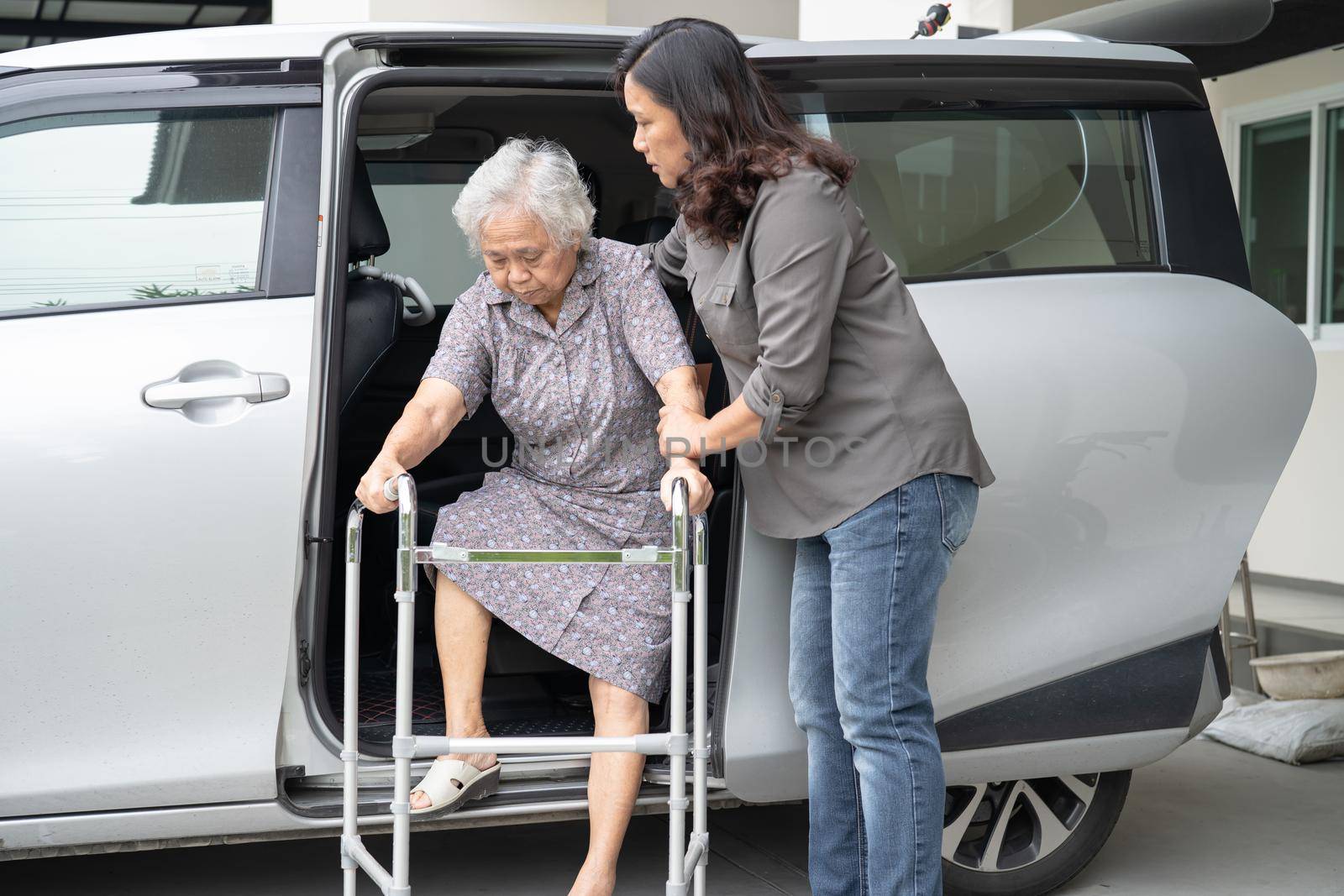 Caregiver daughter help and support asian senior or elderly old lady woman patient prepare get out her car.