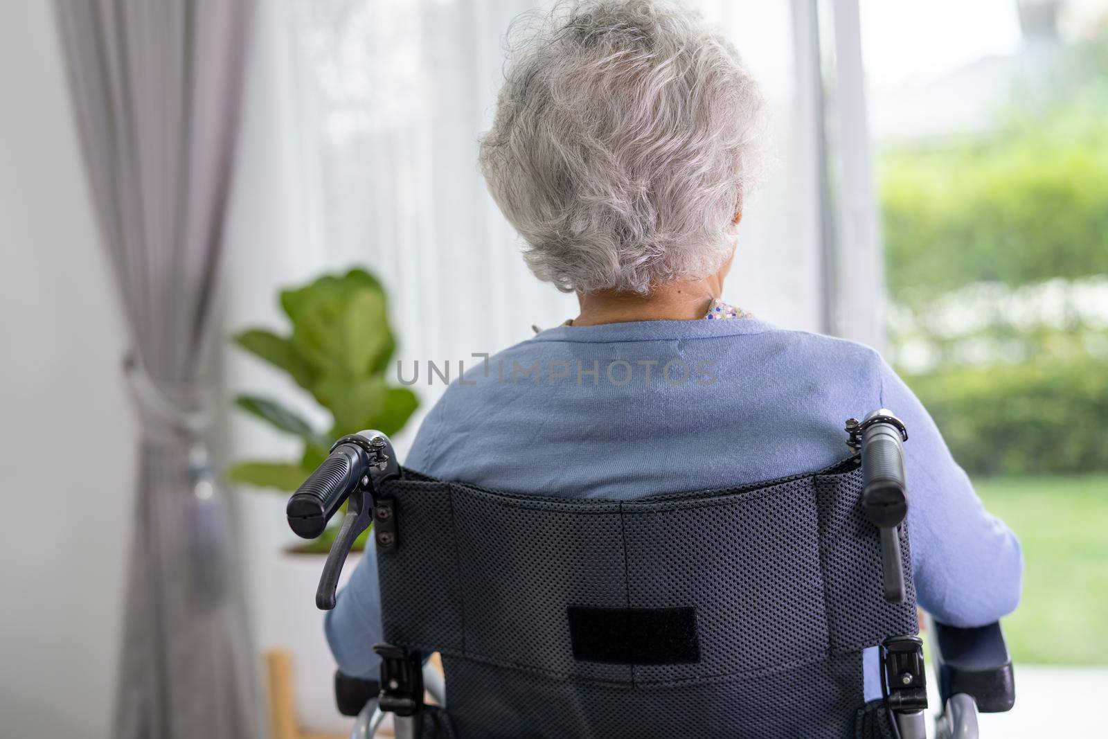 An elderly woman sitting on wheelchair looking out the window for waiting someone. Sadly, melancholy and depressed.