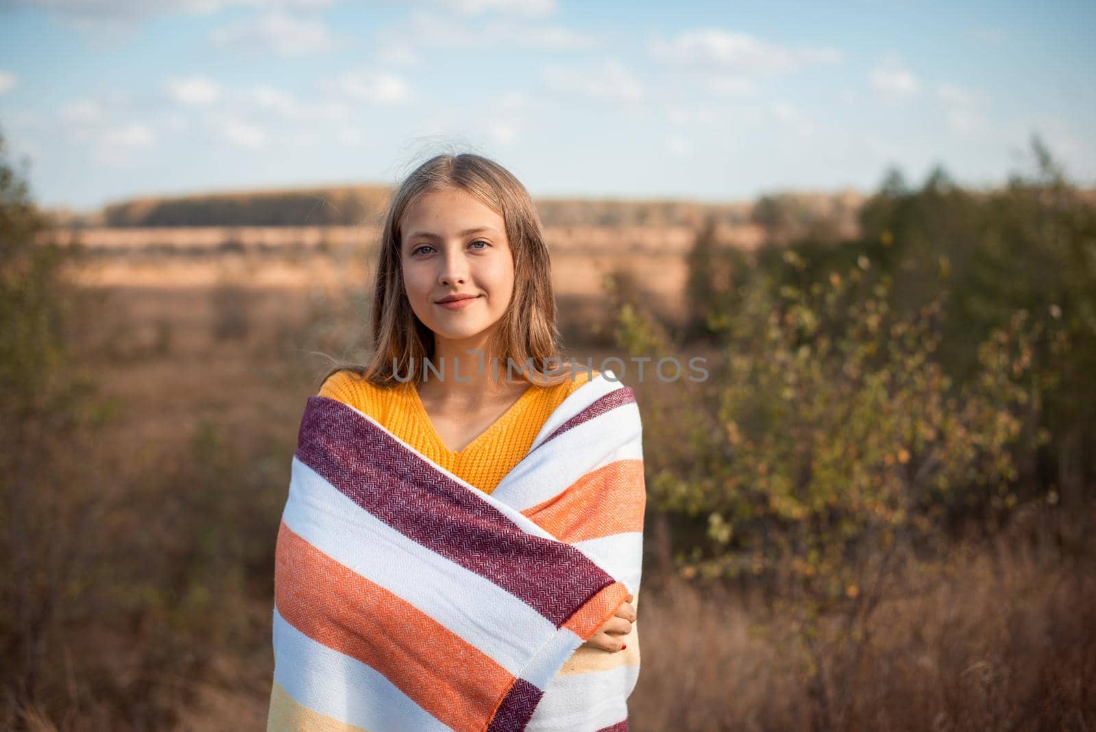 Happy girl in the autumn field wrapped in plaid looking to the camera by VitaliiPetrushenko