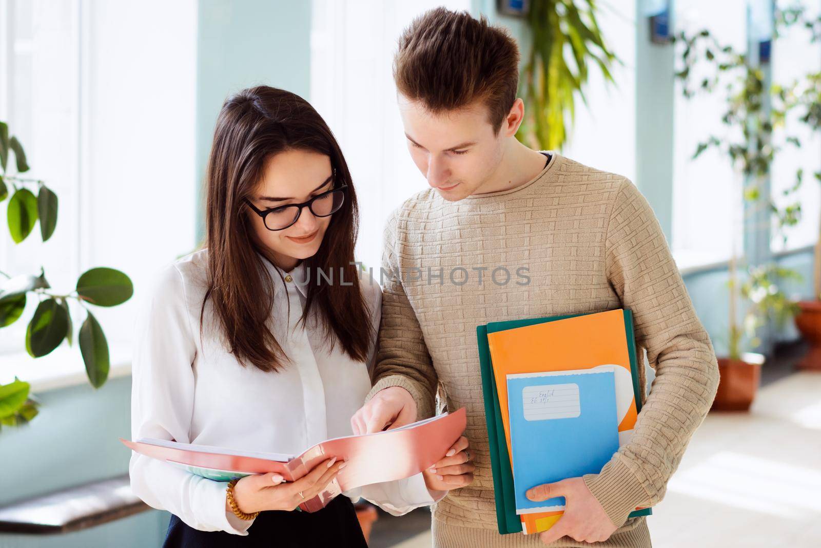 Male and female university students discussing their homework before classes standing in corridor of the university