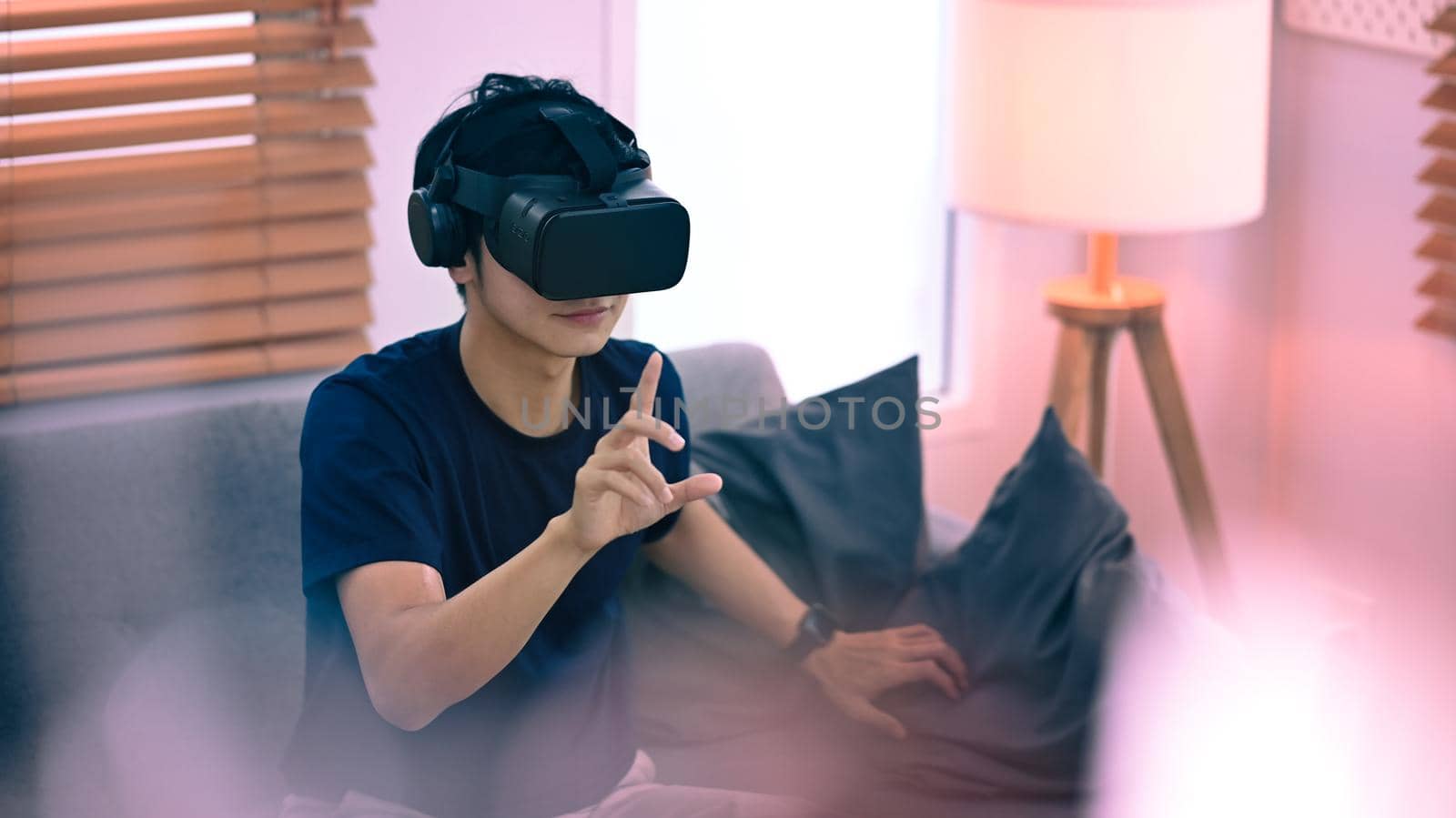Joyful asian man in casual clothes watching movie or play video game on virtual reality headset. Future technology concept by prathanchorruangsak