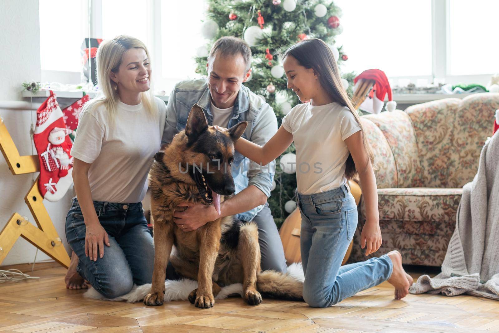 Friendly family is playing with dog near Christmas tree. They are sitting and laughing.