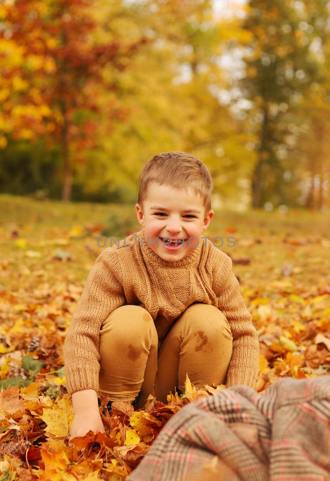 Outdoor fun in autumn. Child playing with autumn fallen leaves in park. Happy little boy
