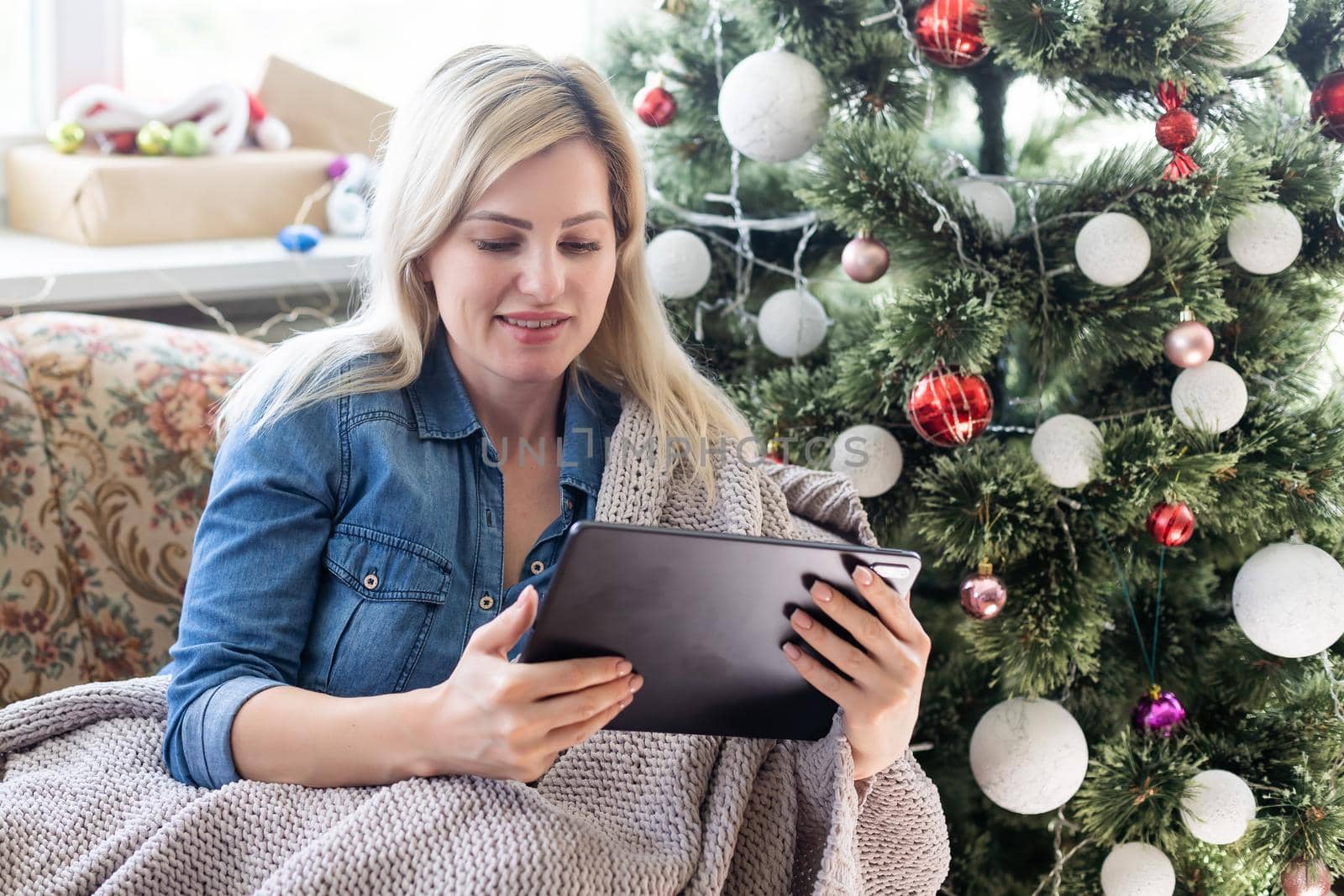 Cute young smiling woman using tablet and happy smiling during cozy Xmas holidays at home