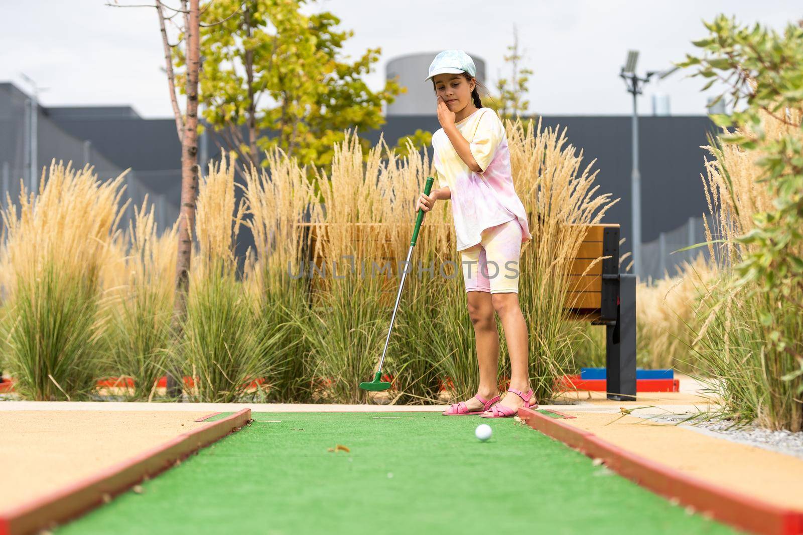 Cute preschool girl playing mini golf with family. Happy child having fun with outdoor activity. Summer sport for children and adults, outdoors. Family vacations or resort