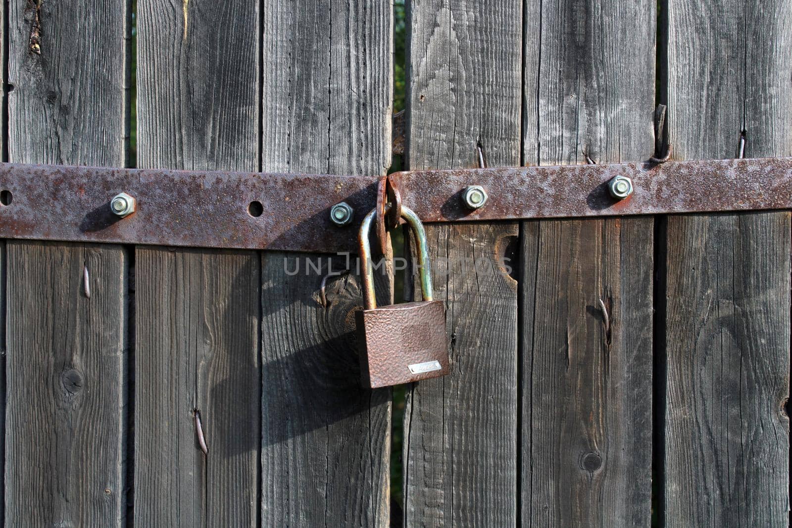 Padlock brown metal lock close-up on old gray wooden gate